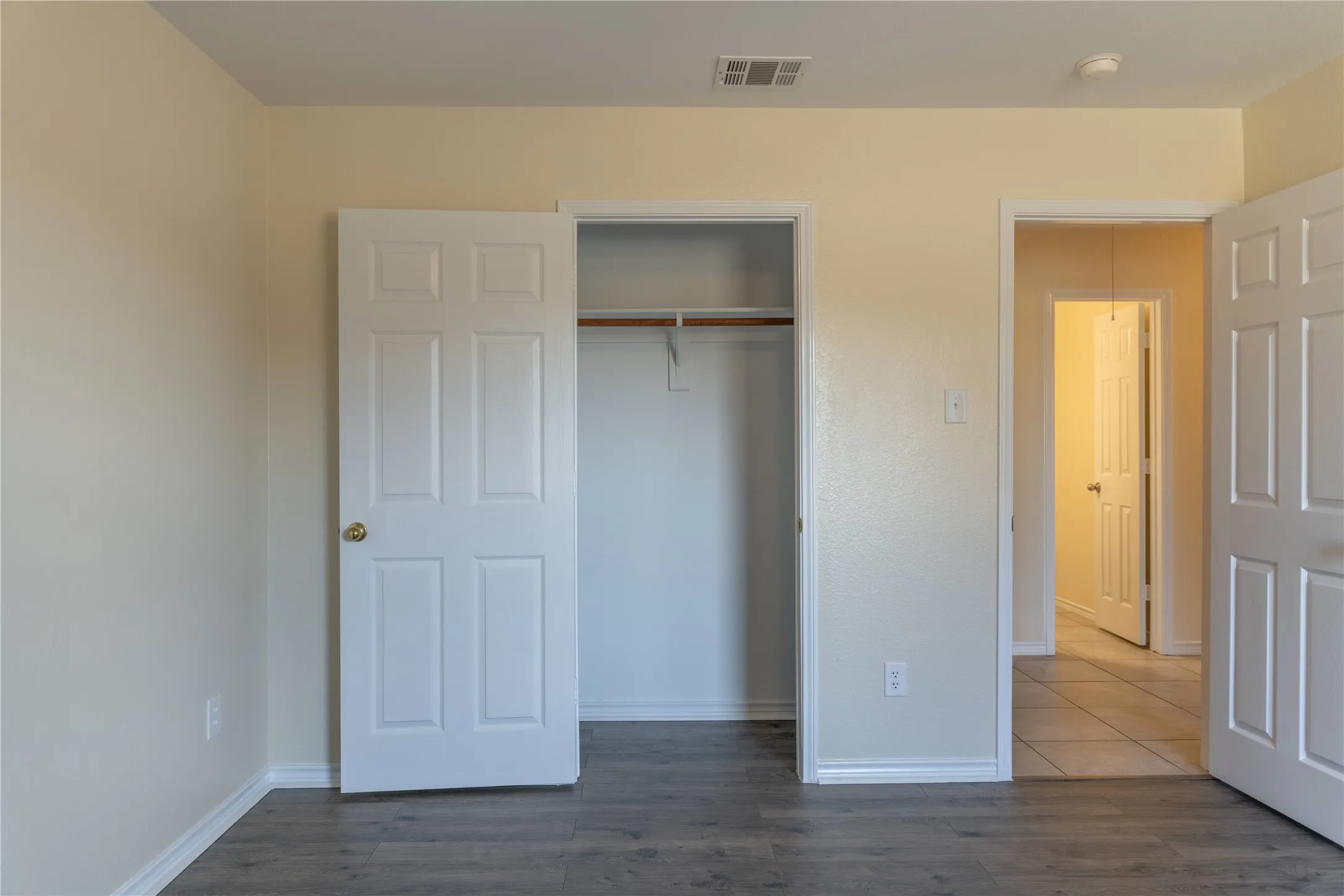 Wood-finish flooring with light-toned walls, white panel doors, and a built-in closet with a hanging rod