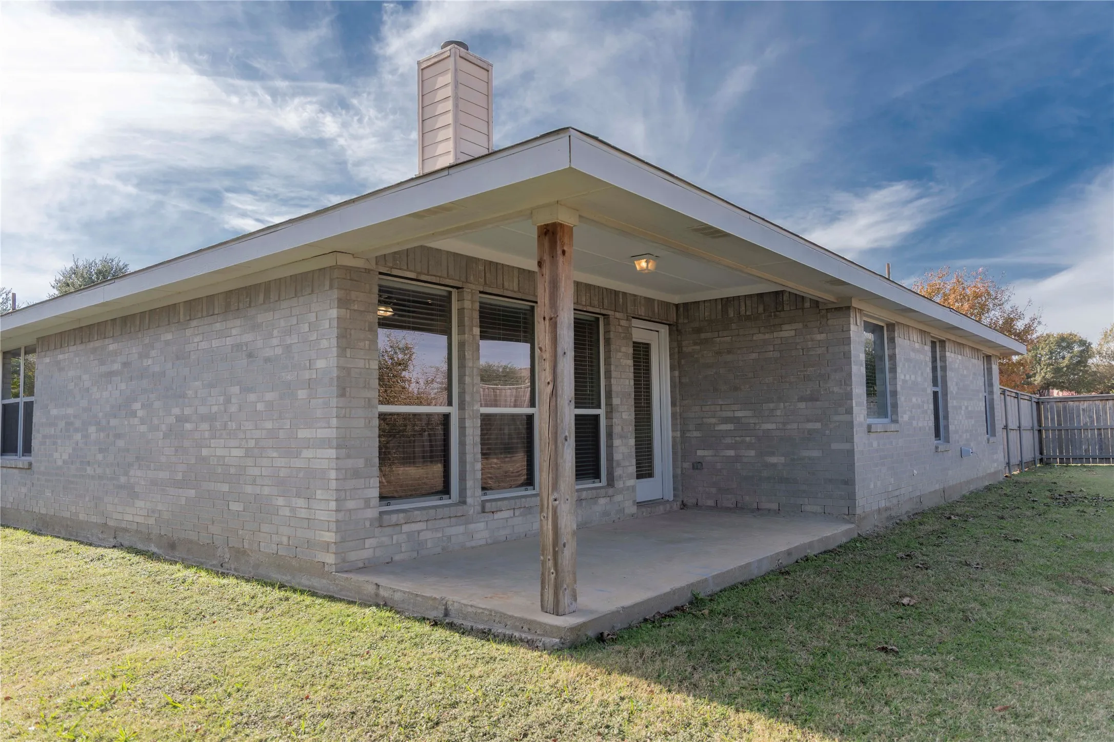 Covered patio with a concrete slab, brick exterior, and a fenced yard