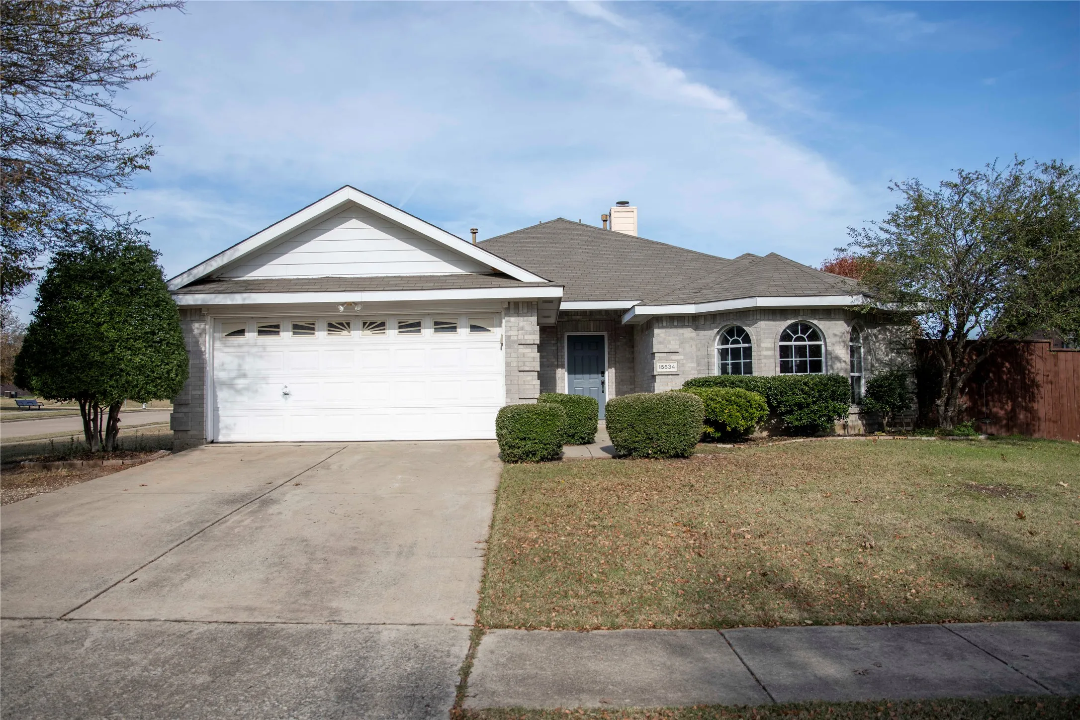 Brick exterior with arched windows, attached two-car garage, and established landscaping