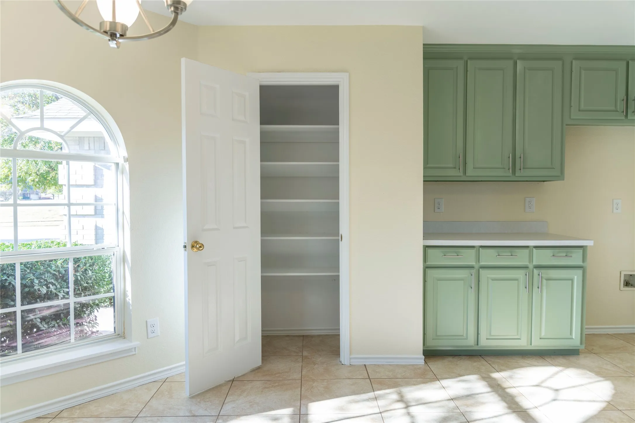 Arched window with grilles, tile flooring, built-in shelving, paneled cabinetry, and a countertop surface