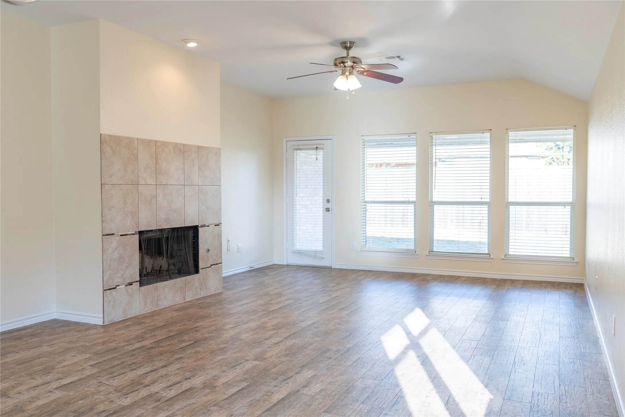 Wood-finish flooring, tiled fireplace, ceiling fan with integrated lighting, vaulted ceiling, and multiple windows