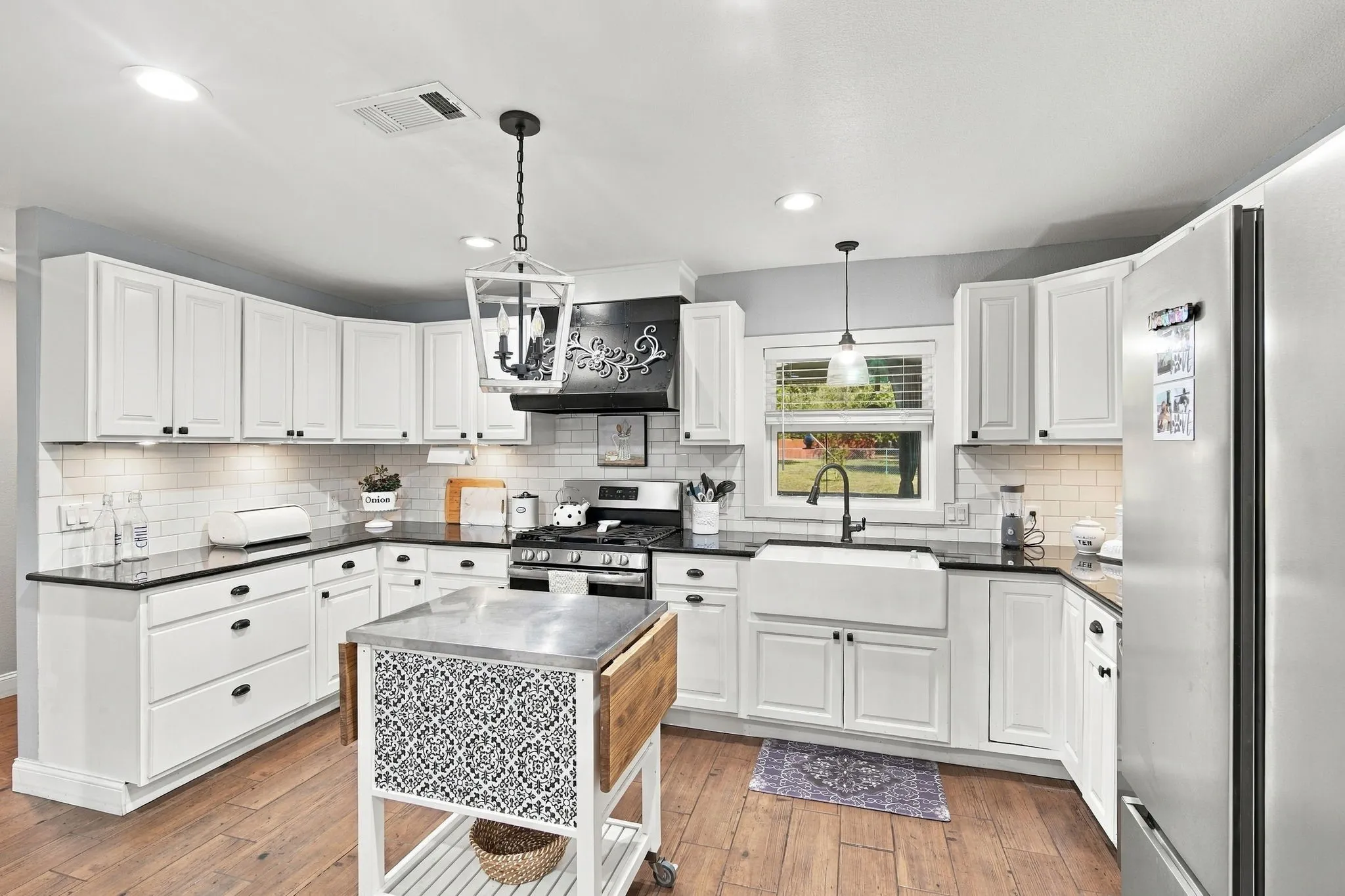 White shaker-style cabinetry with black hardware, black countertops, wood-finish flooring, subway tile backsplash, and a farmhouse sink