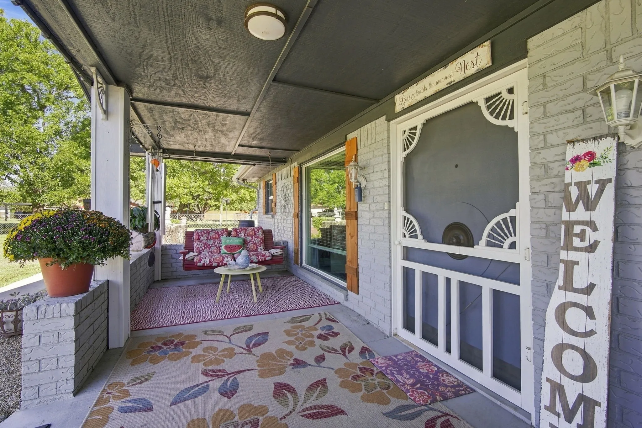 Covered porch with exposed brick, an ornate screen door, and exterior sconce lighting. Yet another space to enjoy the outdoors.