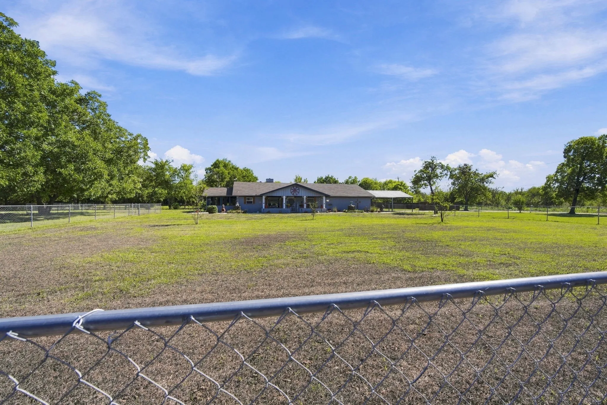 Expansive fenced property with a single-story residence, covered front porch, and mature trees NOTICE the Pecan Trees just outside the fenceline to the left of the property