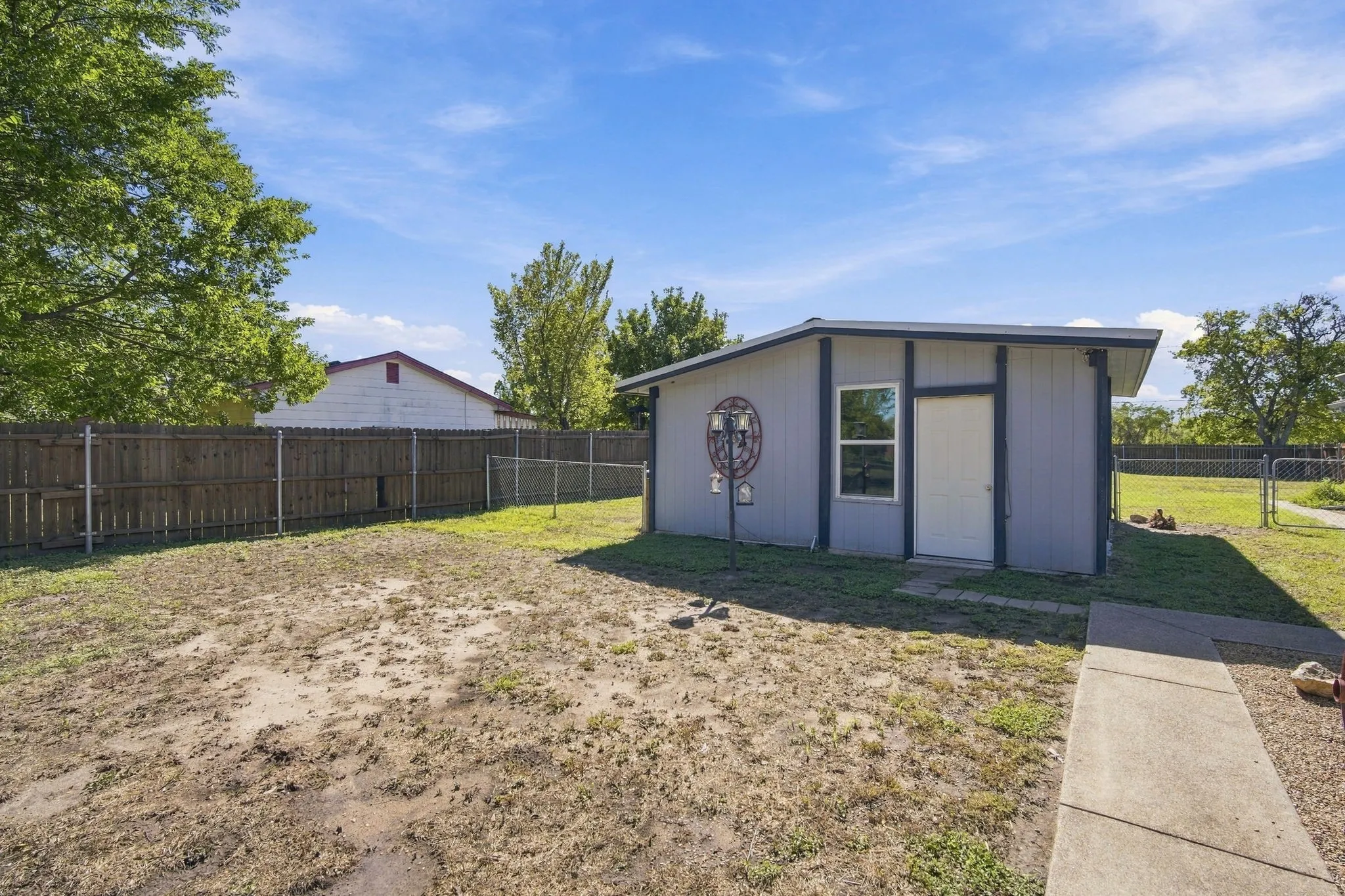 Detached structure with a single window and door, framed by a wood privacy fence and chain link fencing