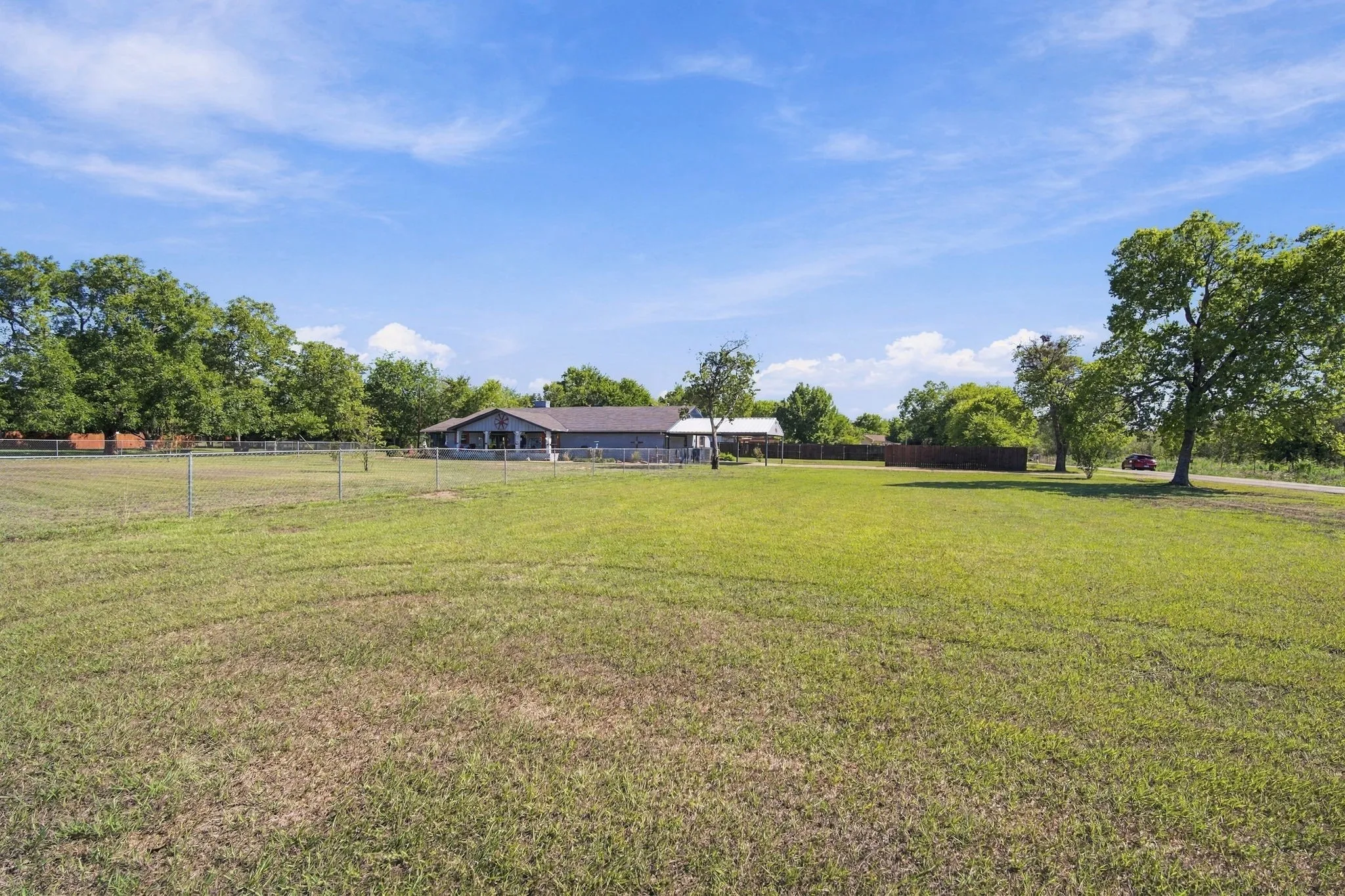 Expansive green space featuring a single-story residence, mature trees, and a perimeter fence