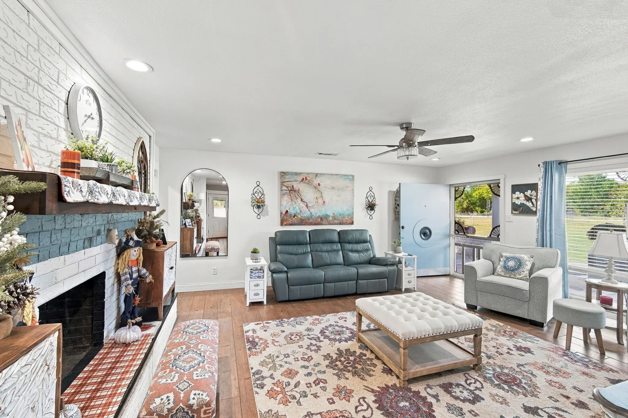 Living area featuring wood-finish flooring, a white brick fireplace, recessed lighting, and a ceiling fan with light