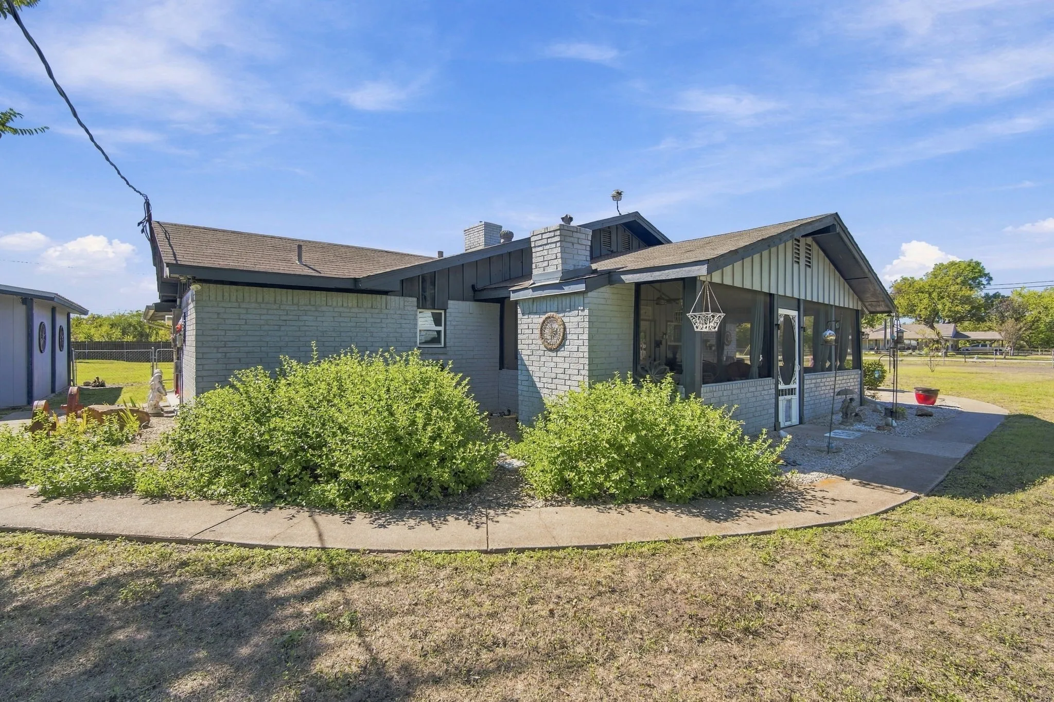 Exterior featuring a gray brick facade, a screened-in porch, a paved walkway, and a detached structure