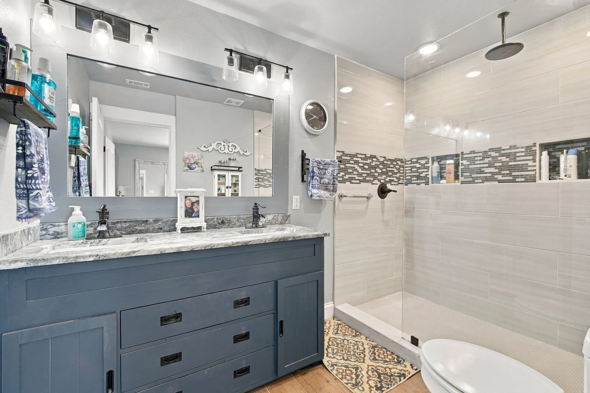 Dual sink vanity with a stone countertop, a large frameless mirror, and track lighting