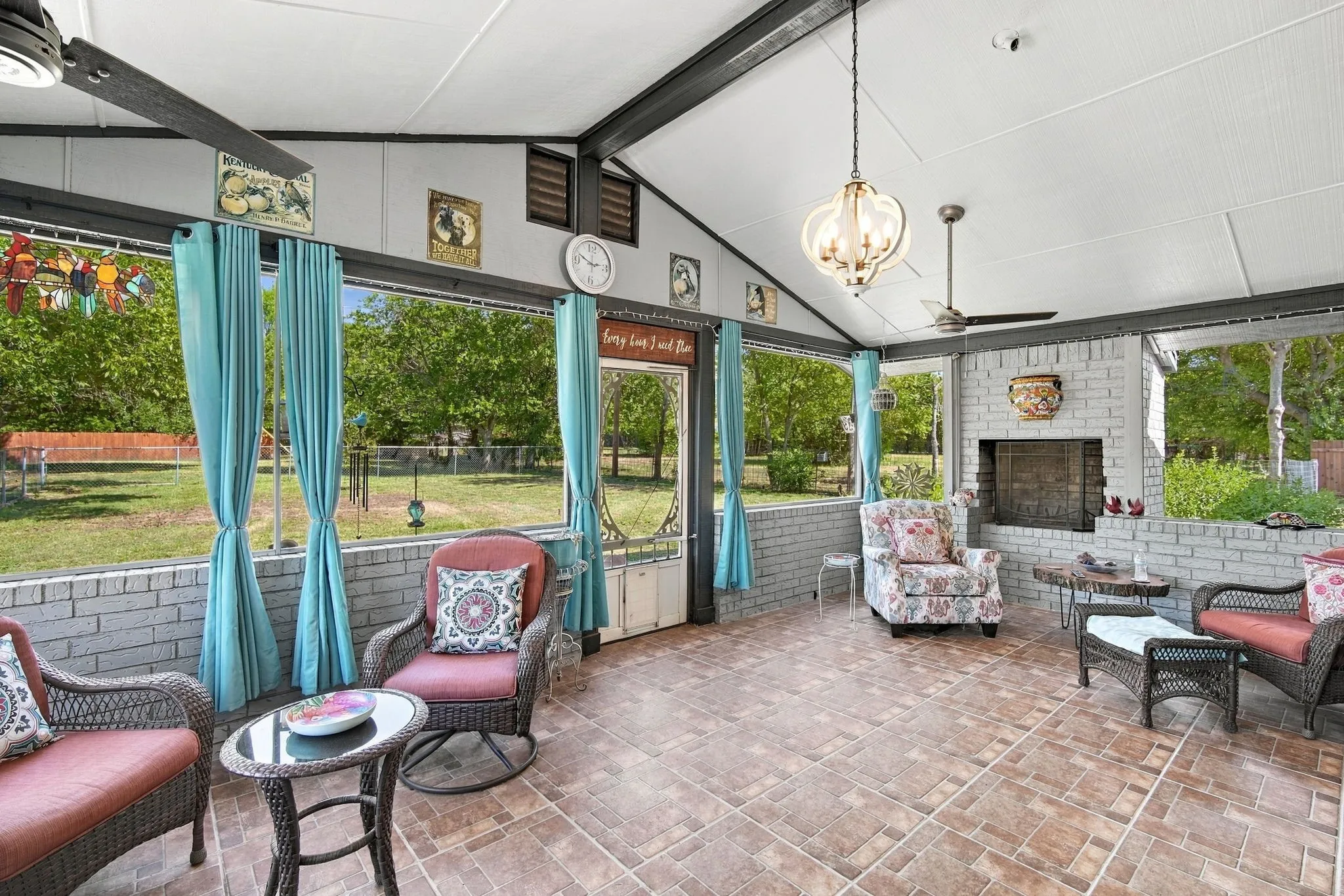 Spacious screened porch featuring a vaulted ceiling, ceiling fans, a decorative chandelier, a brick fireplace, and tile flooring