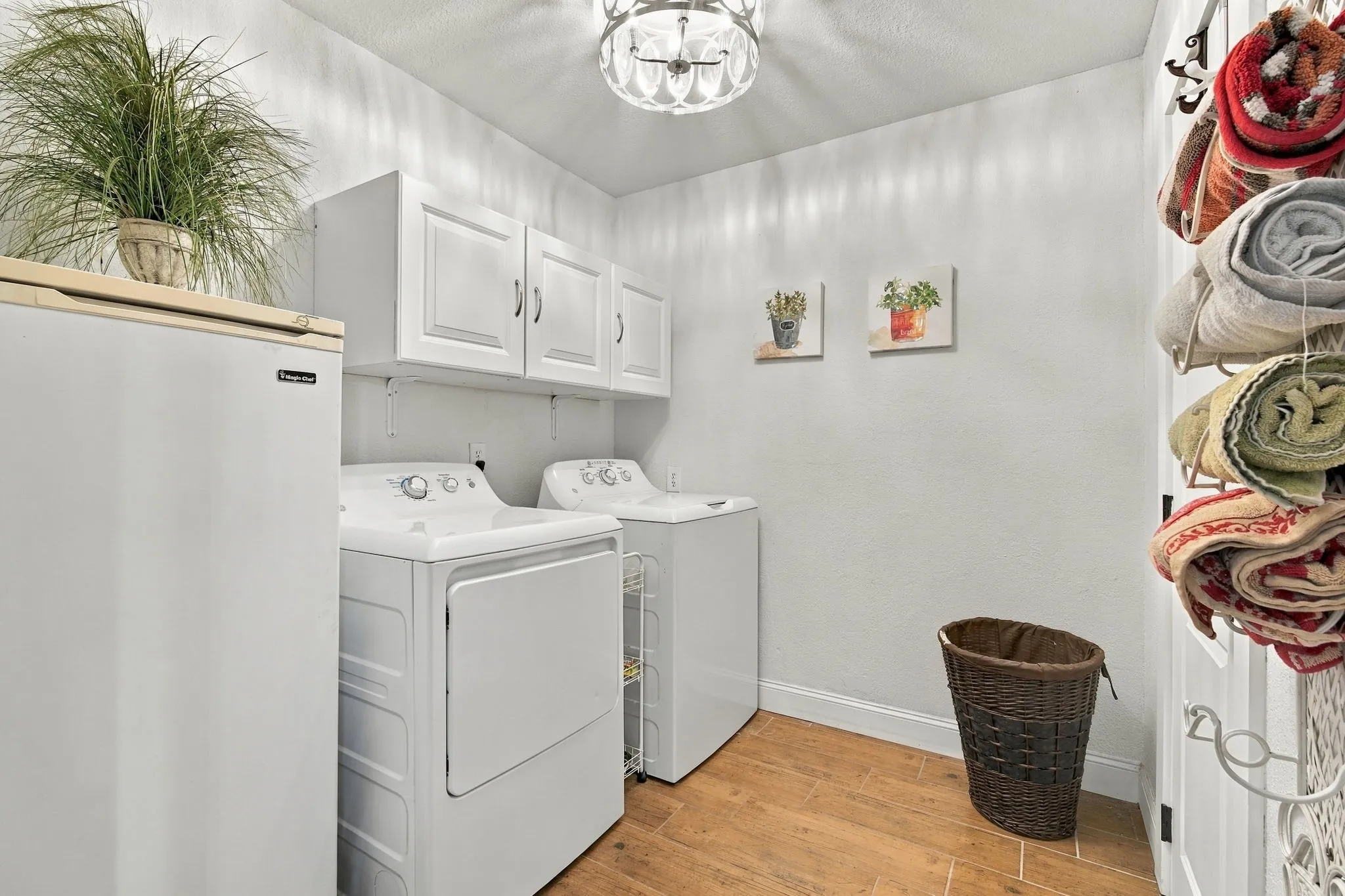 White upper cabinetry, wood-finish flooring, and a decorative ceiling fixture