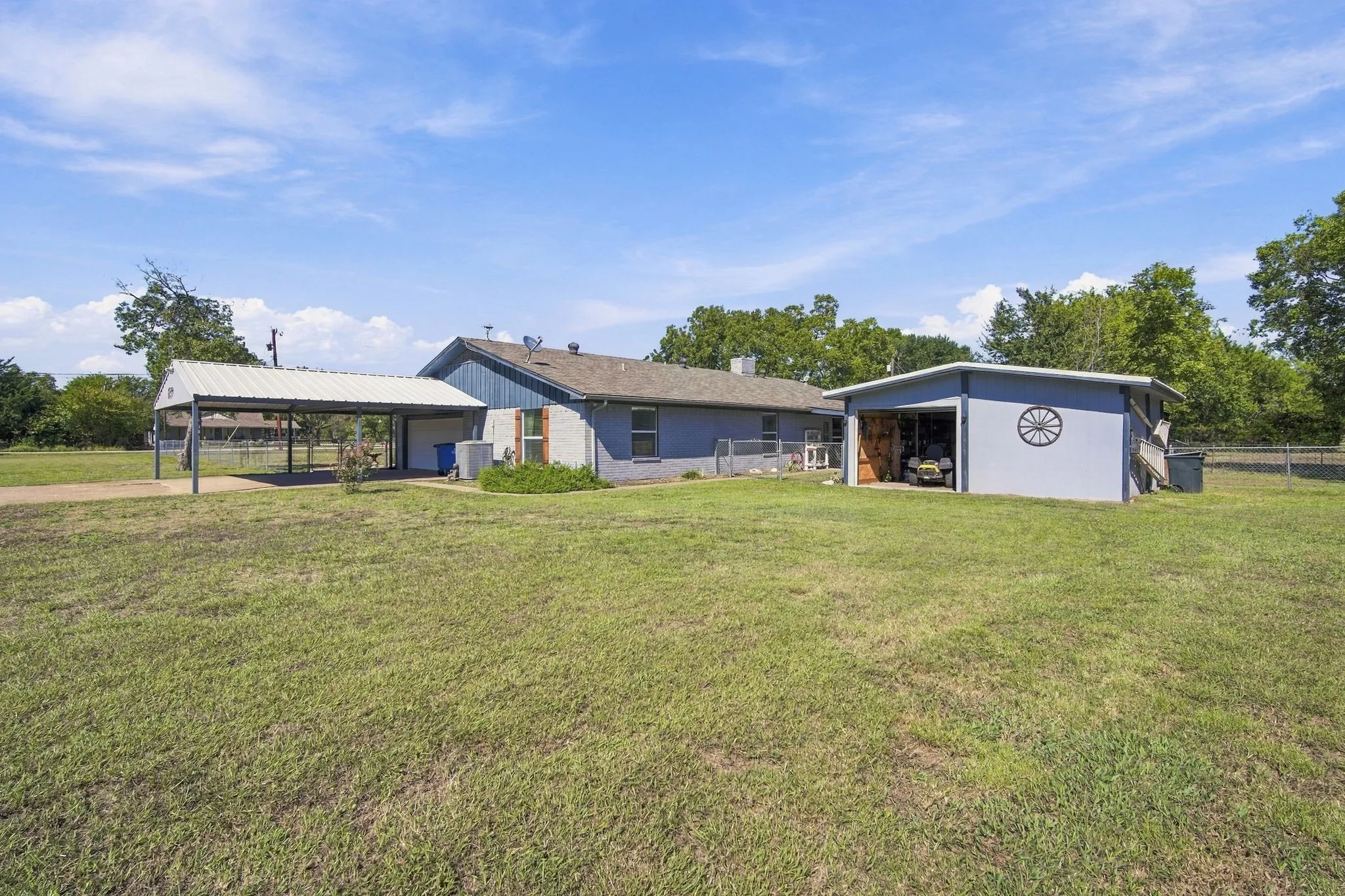 Expansive outdoor space featuring a covered carport, detached storage building, and a fenced area