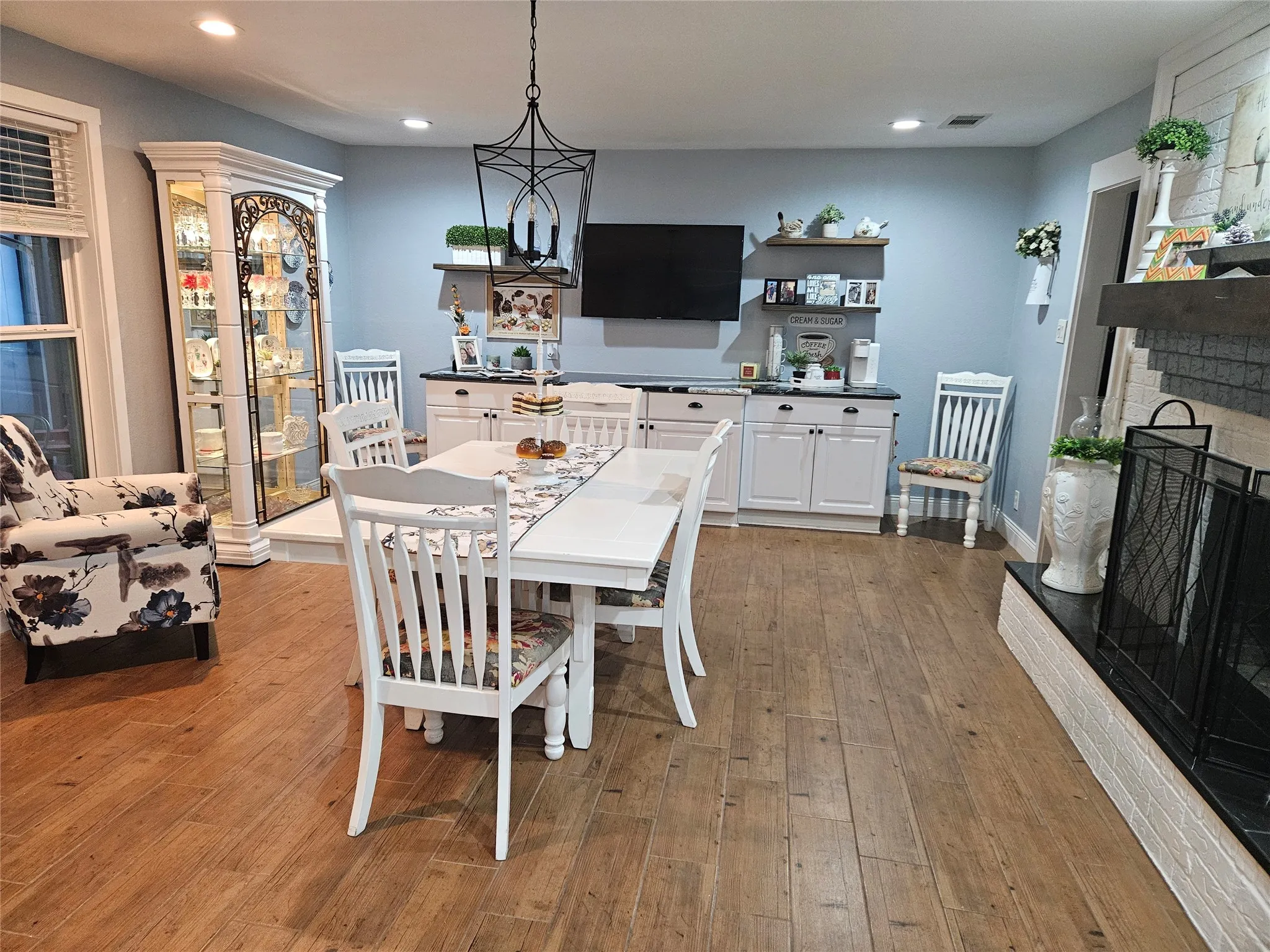 Wood-finish flooring, recessed lighting, built-in cabinetry with dark countertops, a brick fireplace with a black hearth, and a decorative overhead light fixture