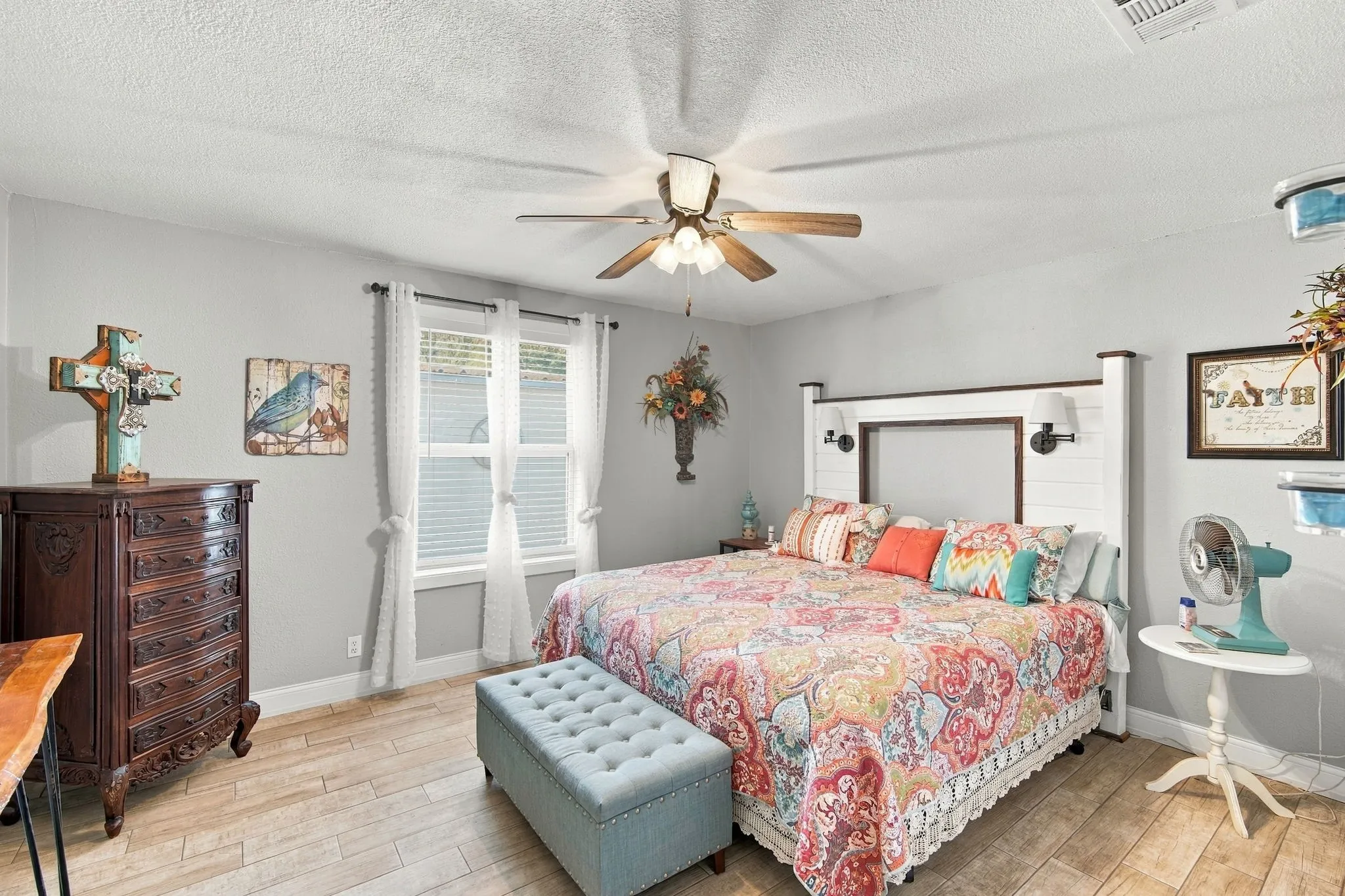 Wood-finish flooring throughout the room, featuring a window with blinds, and a ceiling fan with integrated lighting