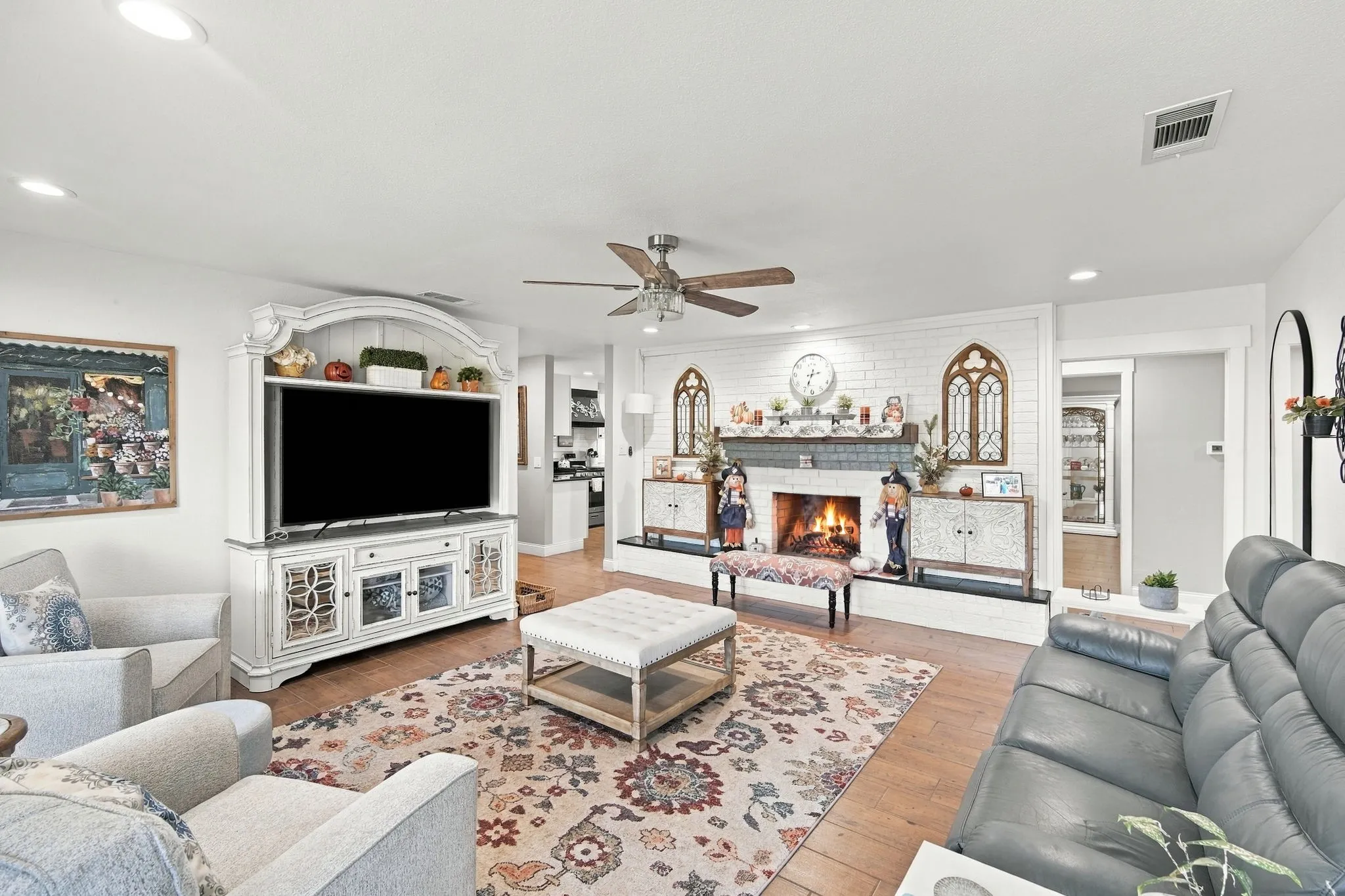 Living area featuring wood-finish flooring, a white brick fireplace with a mantel, and recessed lighting