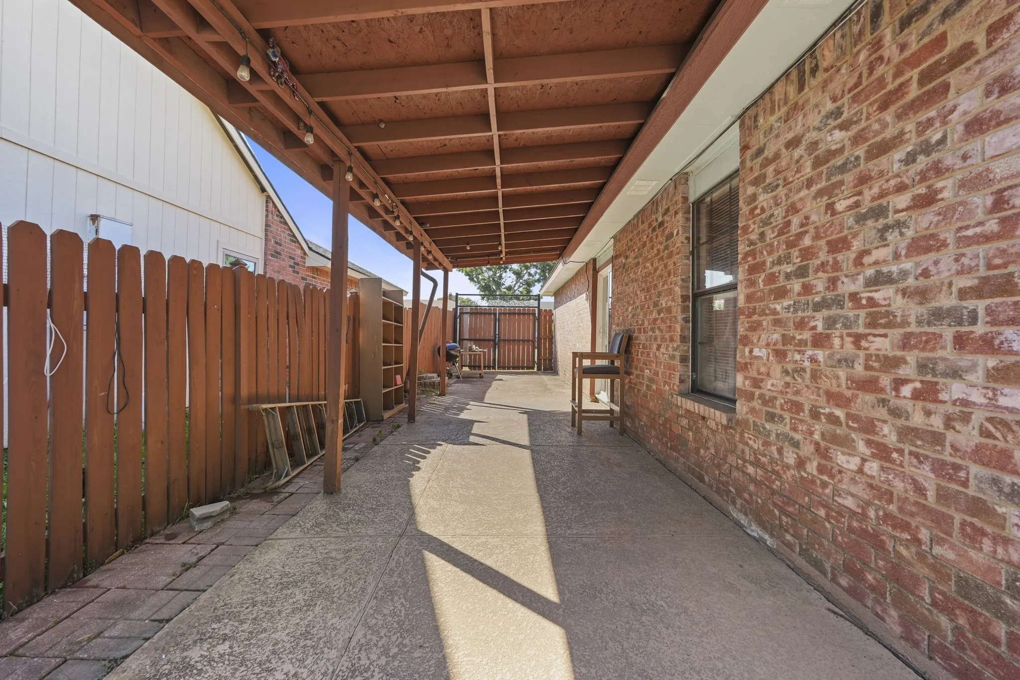 Covered patio with a concrete surface, wooden fence, brick exterior, and multi-pane windows