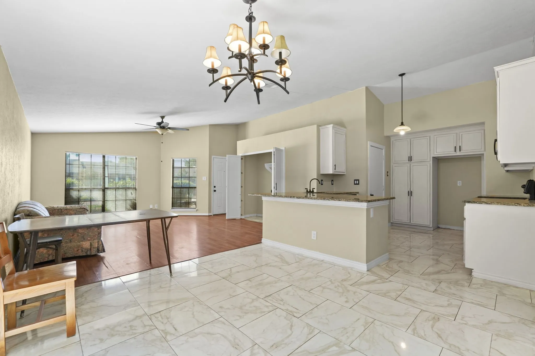 Open-concept living area featuring large windows, wood-finish flooring, and a kitchen with white cabinetry and granite countertops