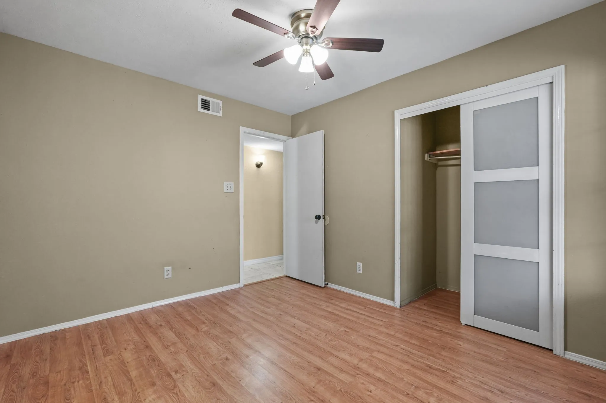Wood-finish flooring, ceiling fan with light fixture, built-in closet with sliding doors, and neutral wall tones