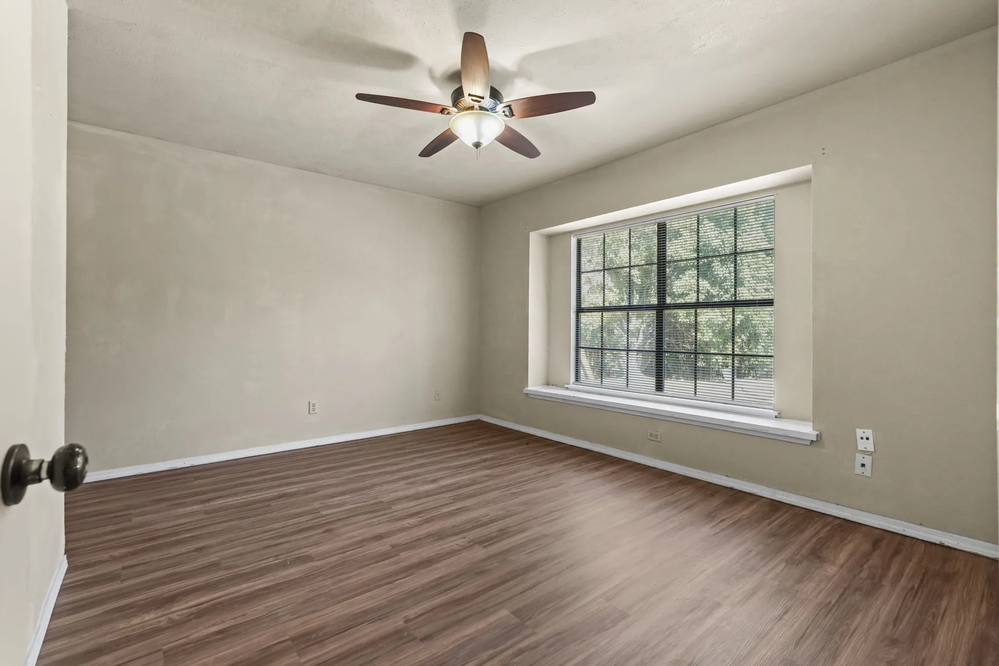 Wood-finish flooring, ceiling fan with integrated lighting, and a large window with grilles
