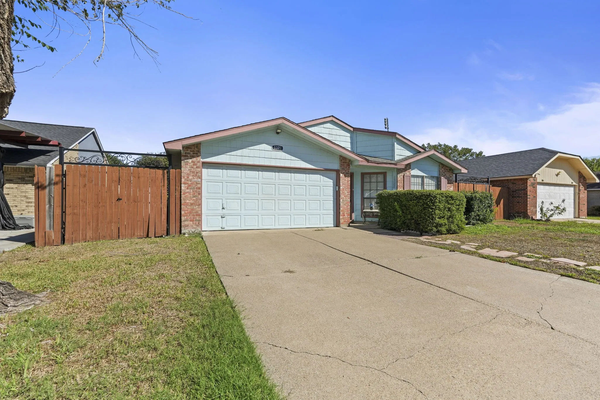 Brick and siding exterior with a light blue garage door, concrete driveway, and mature landscaping