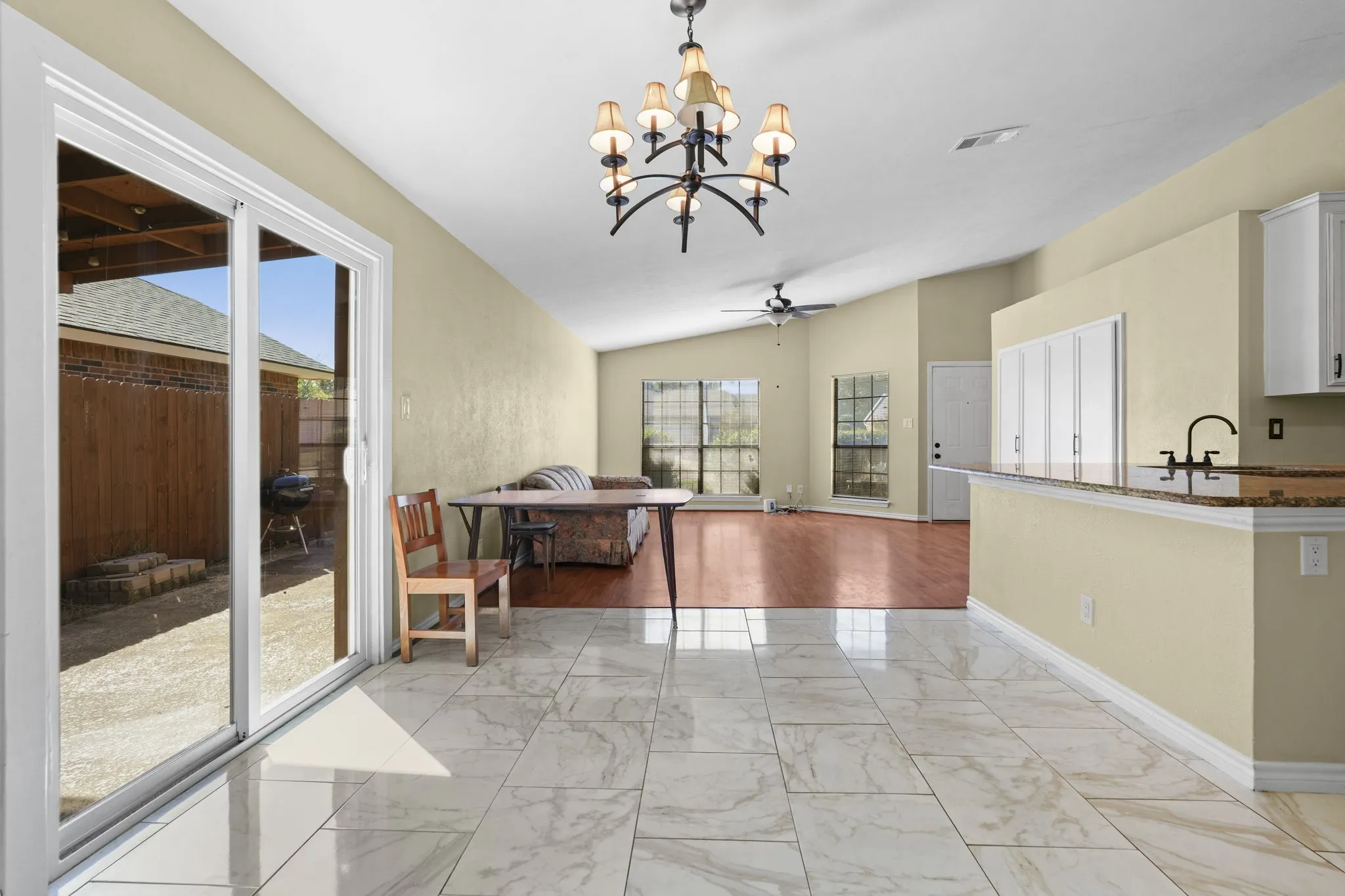 Marble-look tile flooring, vaulted ceiling, wood-finish flooring, sliding glass patio door, and a built-in breakfast bar with a stone countertop