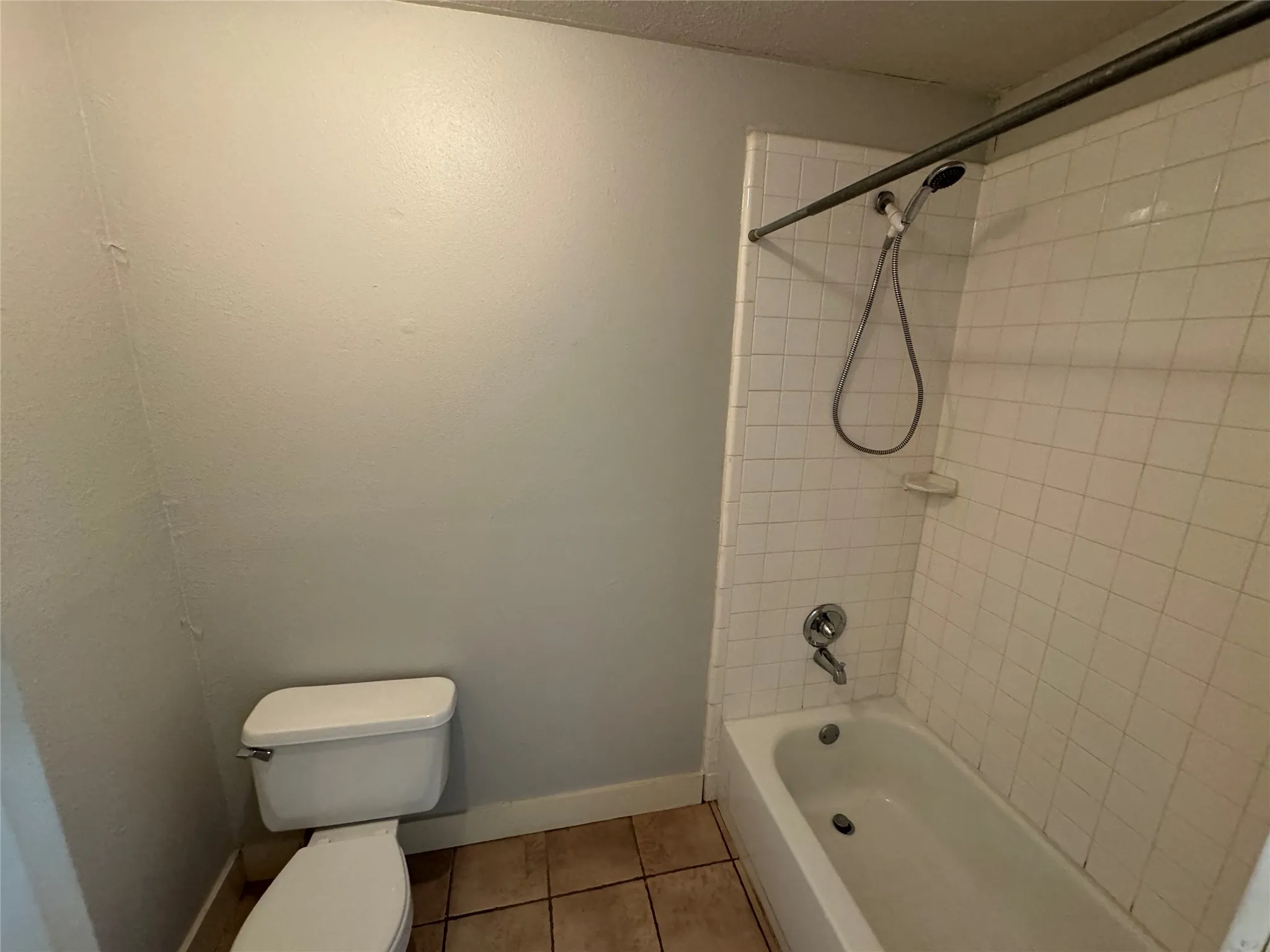 Bathroom featuring tiled shower / bath, toilet, and tile patterned floors