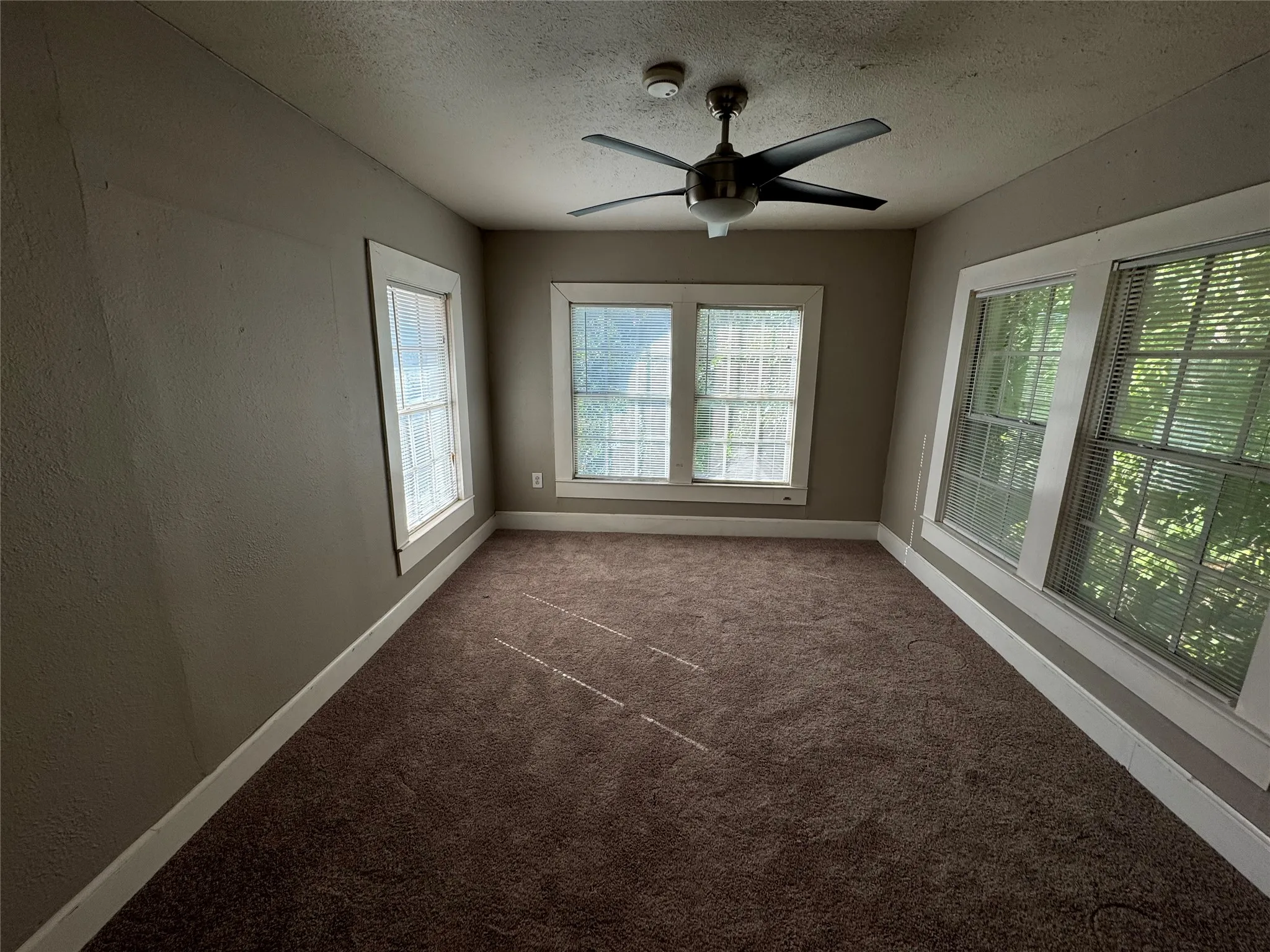 Unfurnished room with dark carpet, ceiling fan, and a textured ceiling