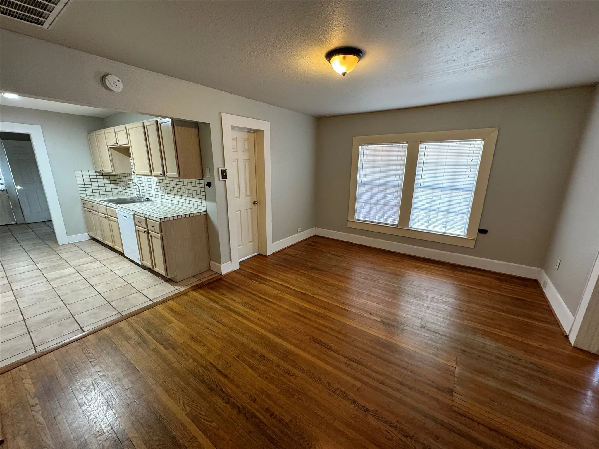 Kitchen featuring a textured ceiling, dishwasher, light hardwood / wood-style floors, sink, and decorative backsplash