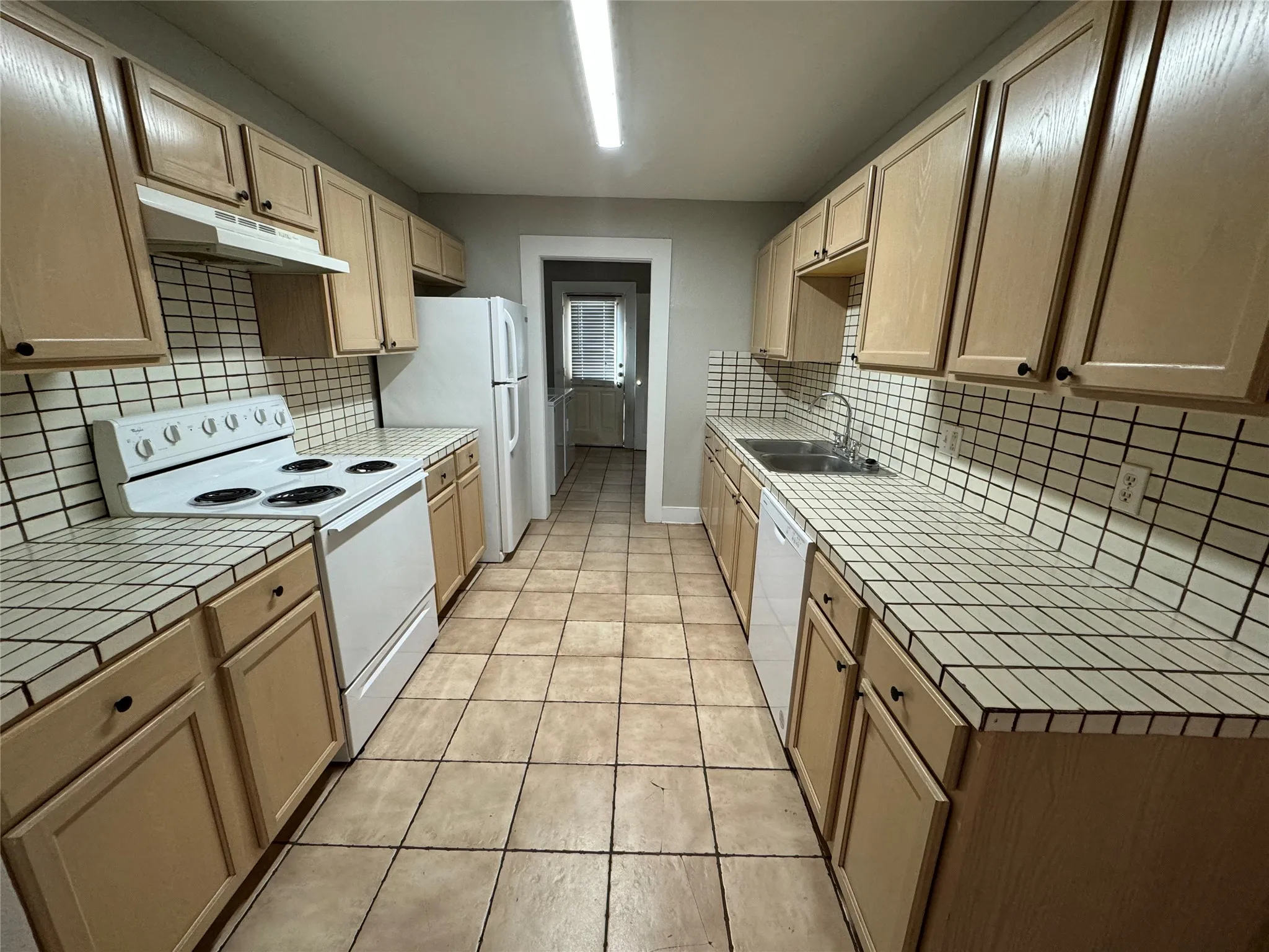 Kitchen featuring white appliances, light tile patterned floors, decorative backsplash, and sink
