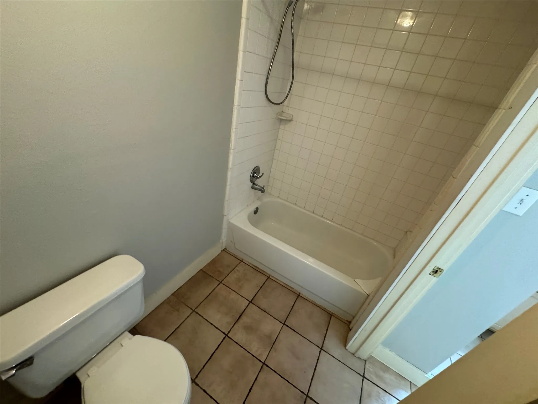 Bathroom featuring tiled shower / bath, toilet, and tile patterned flooring