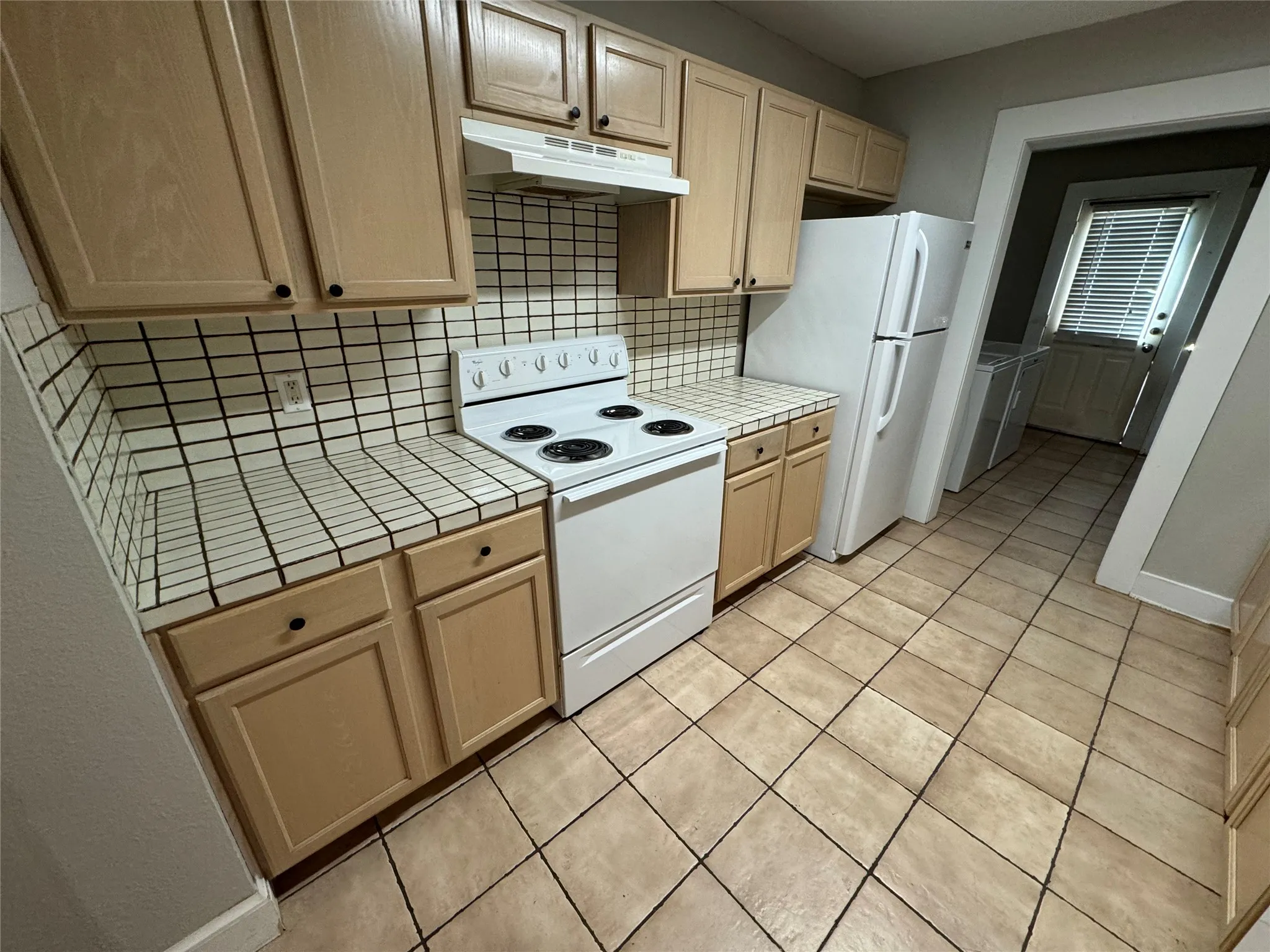 Kitchen featuring white appliances, light tile patterned floors, light brown cabinets, and tasteful backsplash