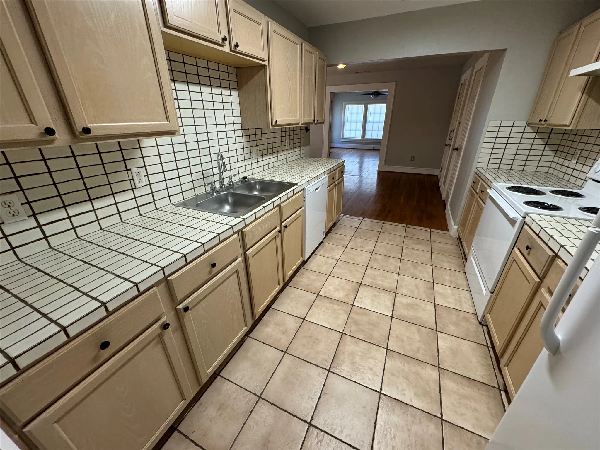 Kitchen with white appliances, light hardwood / wood-style flooring, tile countertops, sink, and decorative backsplash