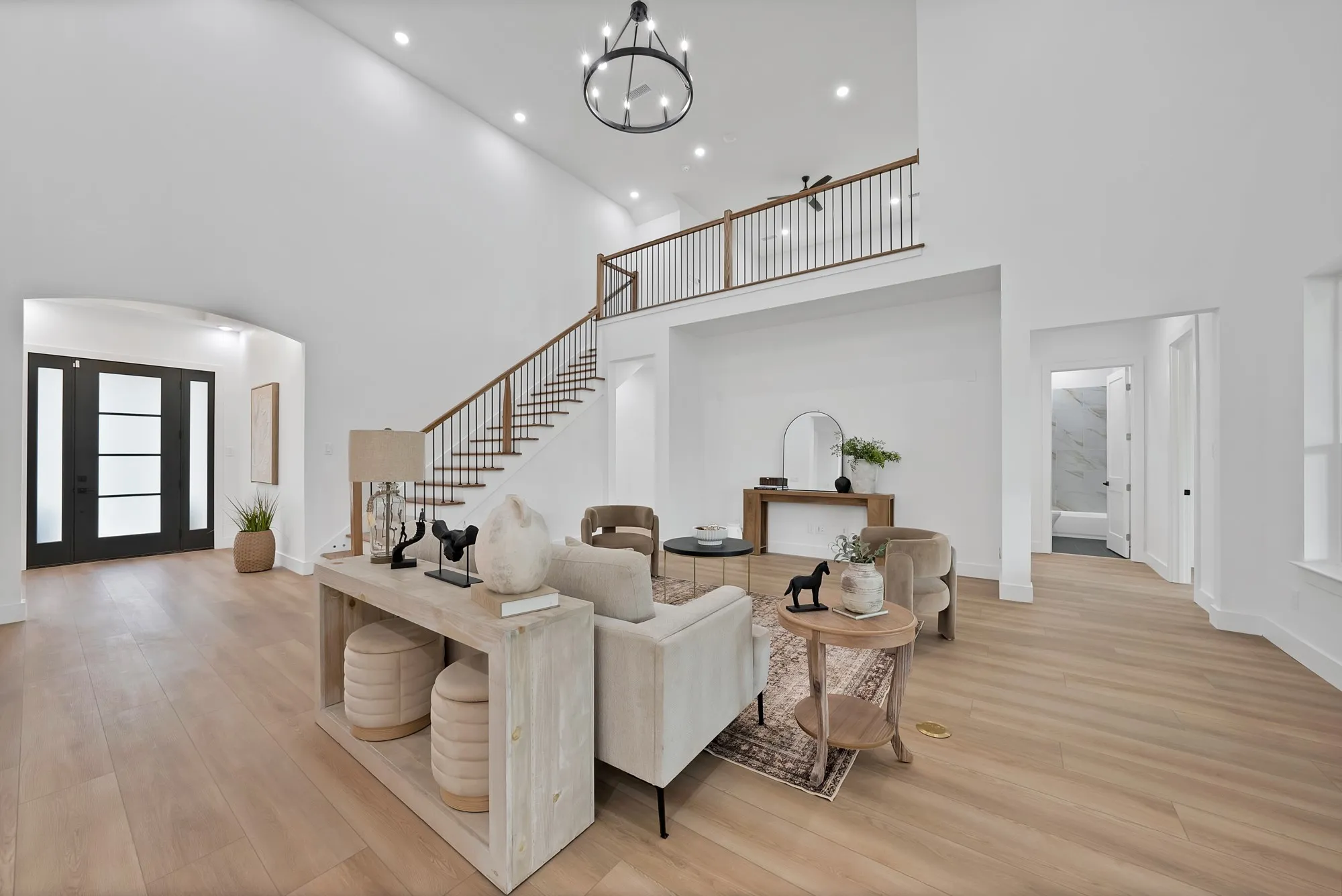 Two-story entry foyer with a dark-framed glass paneled door, wood-finish flooring, and a staircase featuring dark wood treads and a black metal railing