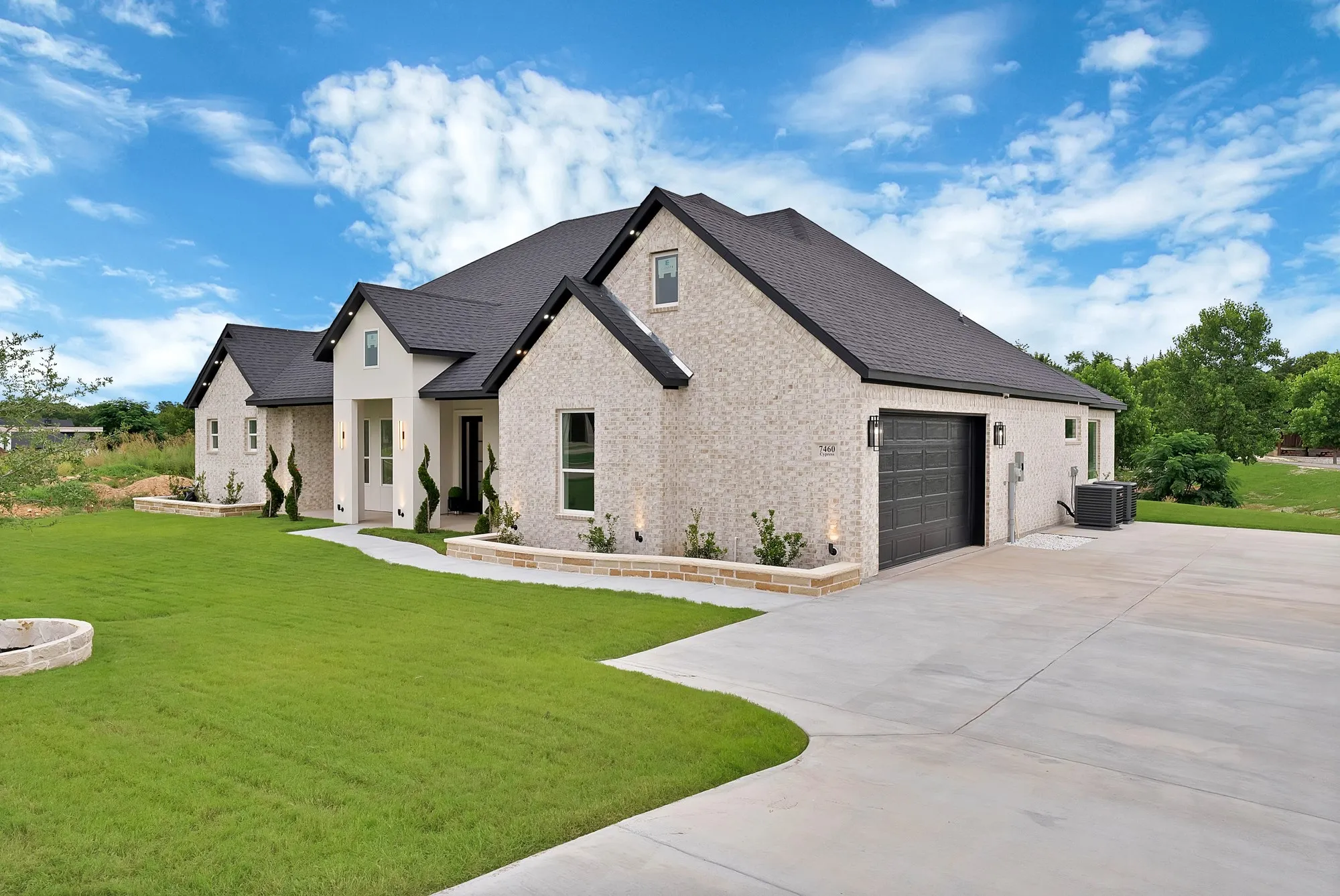 Light brick exterior with contrasting dark roof, attached two-car garage, concrete driveway, and manicured lawn
