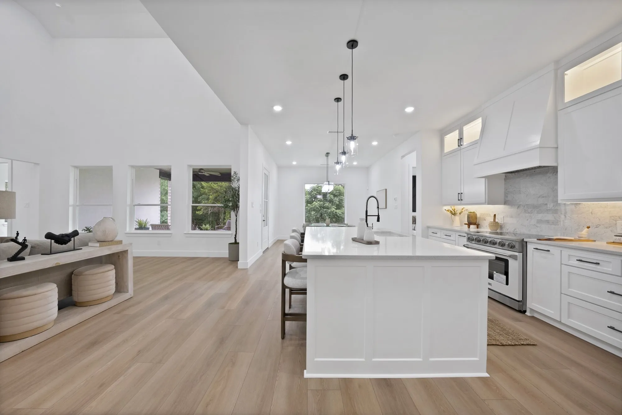 Open-concept design featuring vaulted ceilings, wood-finish flooring, a kitchen island with pendant lighting, white cabinetry, and stainless steel appliances