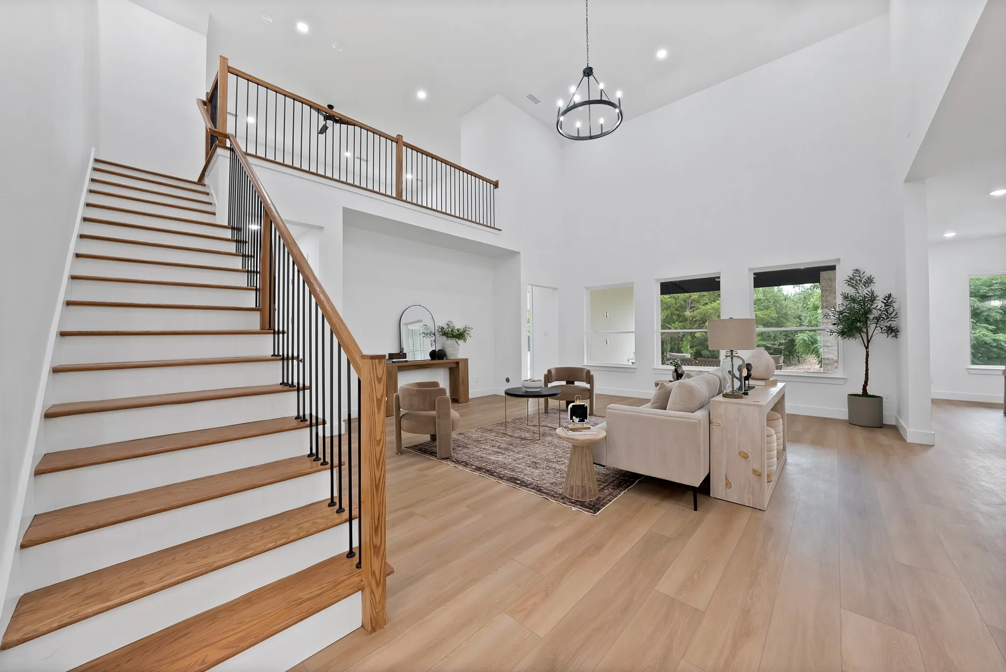 Two-story living area with high ceilings, wood-finish flooring, and an open staircase with a wood handrail and black metal spindles