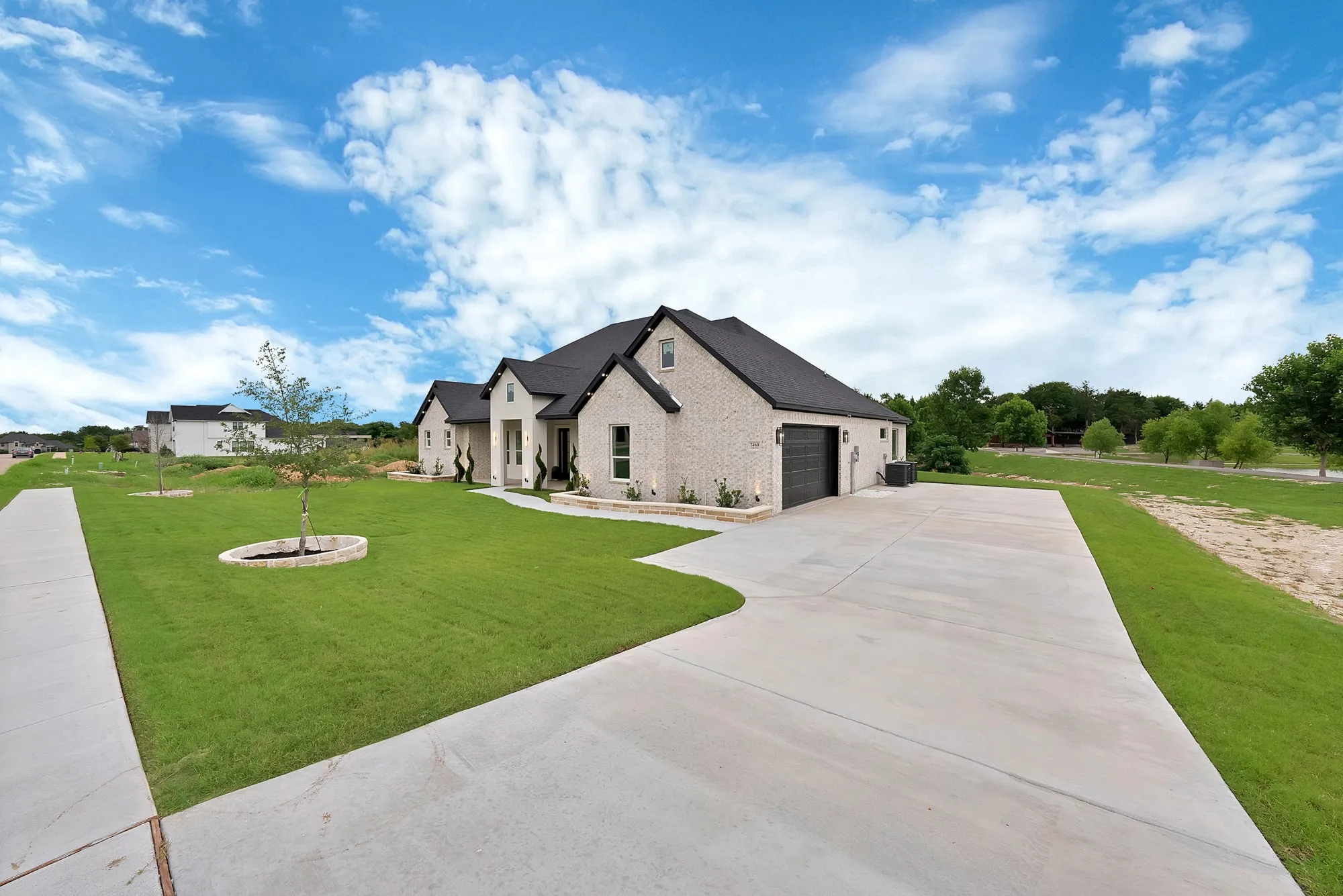 Contemporary exterior featuring light-colored brick, dark roof, dark garage door, extensive concrete driveway, and a manicured lawn