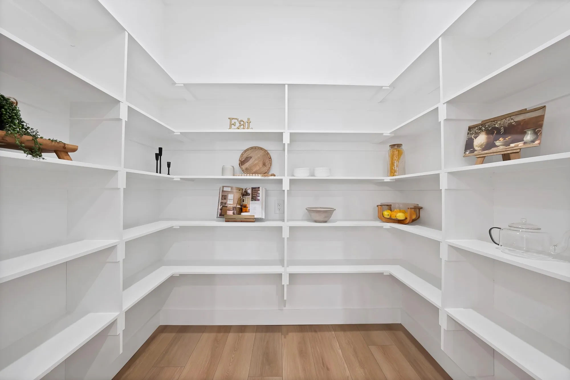 Expansive pantry with extensive white shelving, wood-finish flooring, and bright illumination