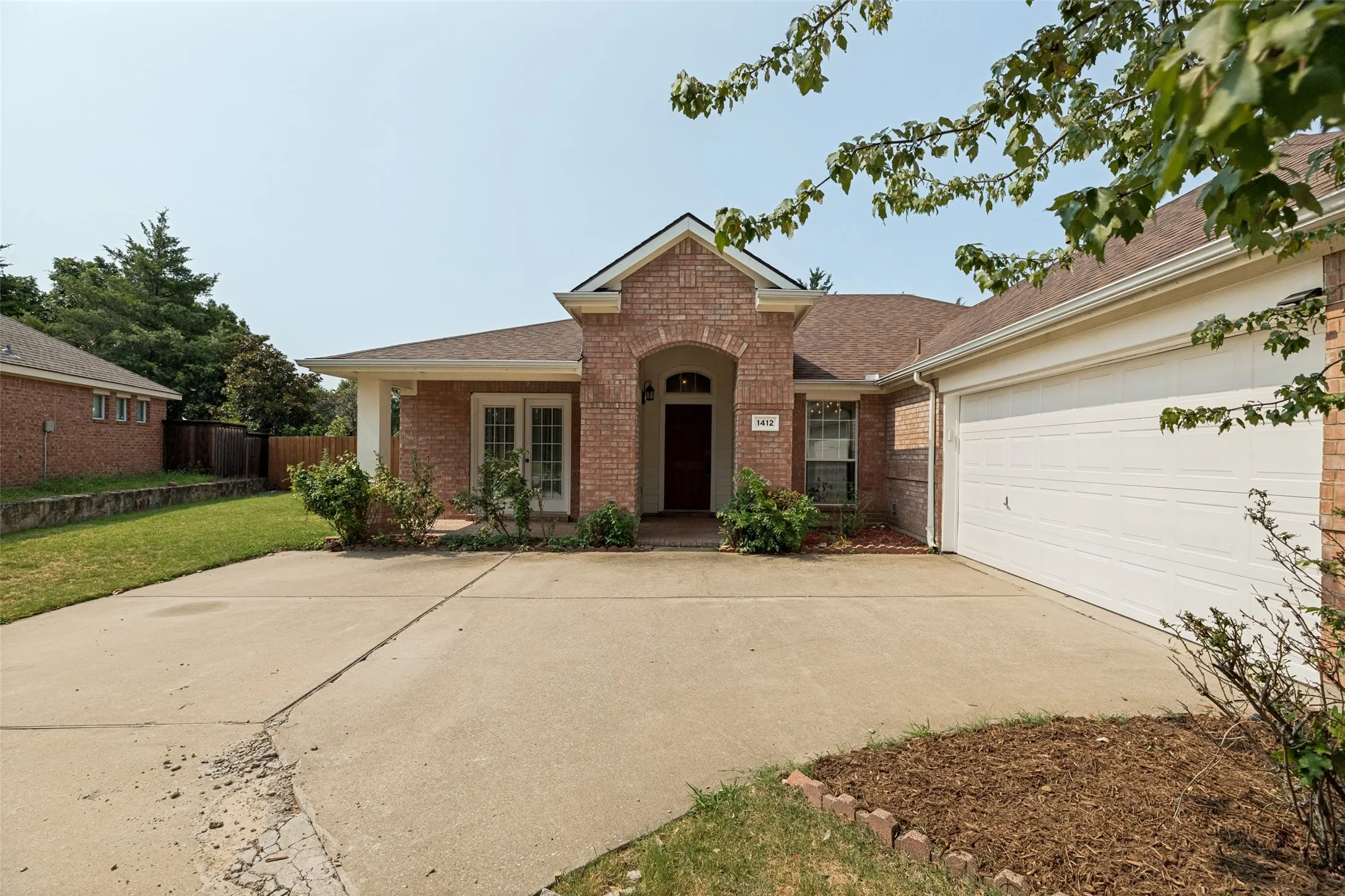 Brick exterior with an arched entryway, attached two-car garage, and a concrete driveway