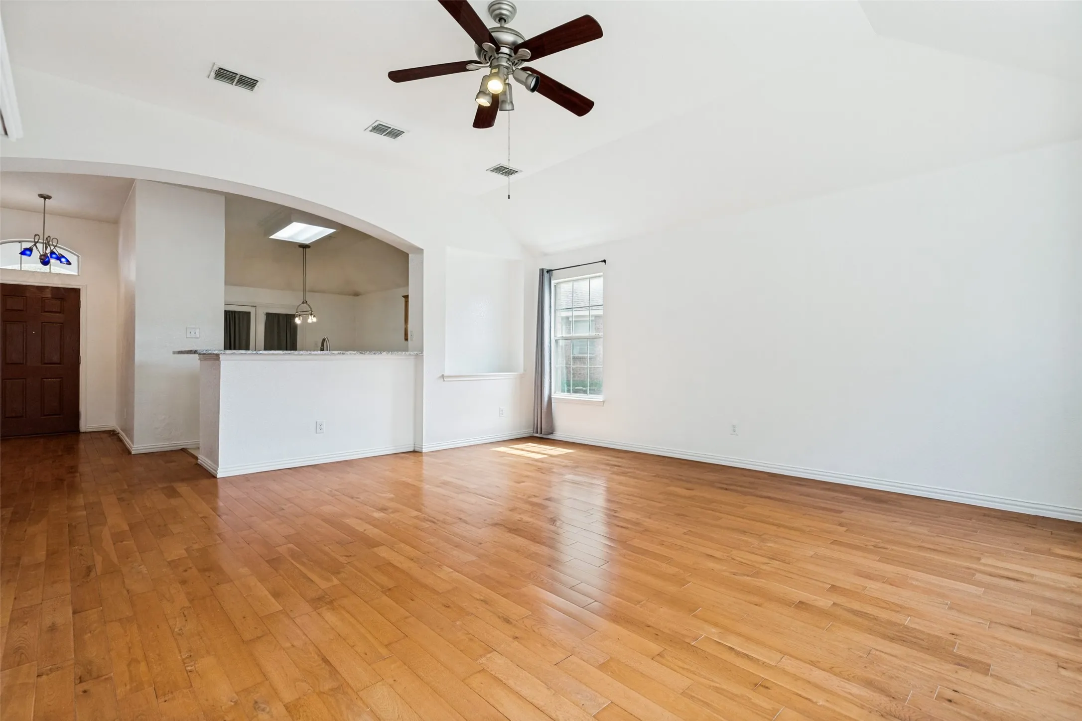 Vaulted ceiling with a ceiling fan, wood-finish flooring, arched doorway, pass-through counter, and a window with curtains