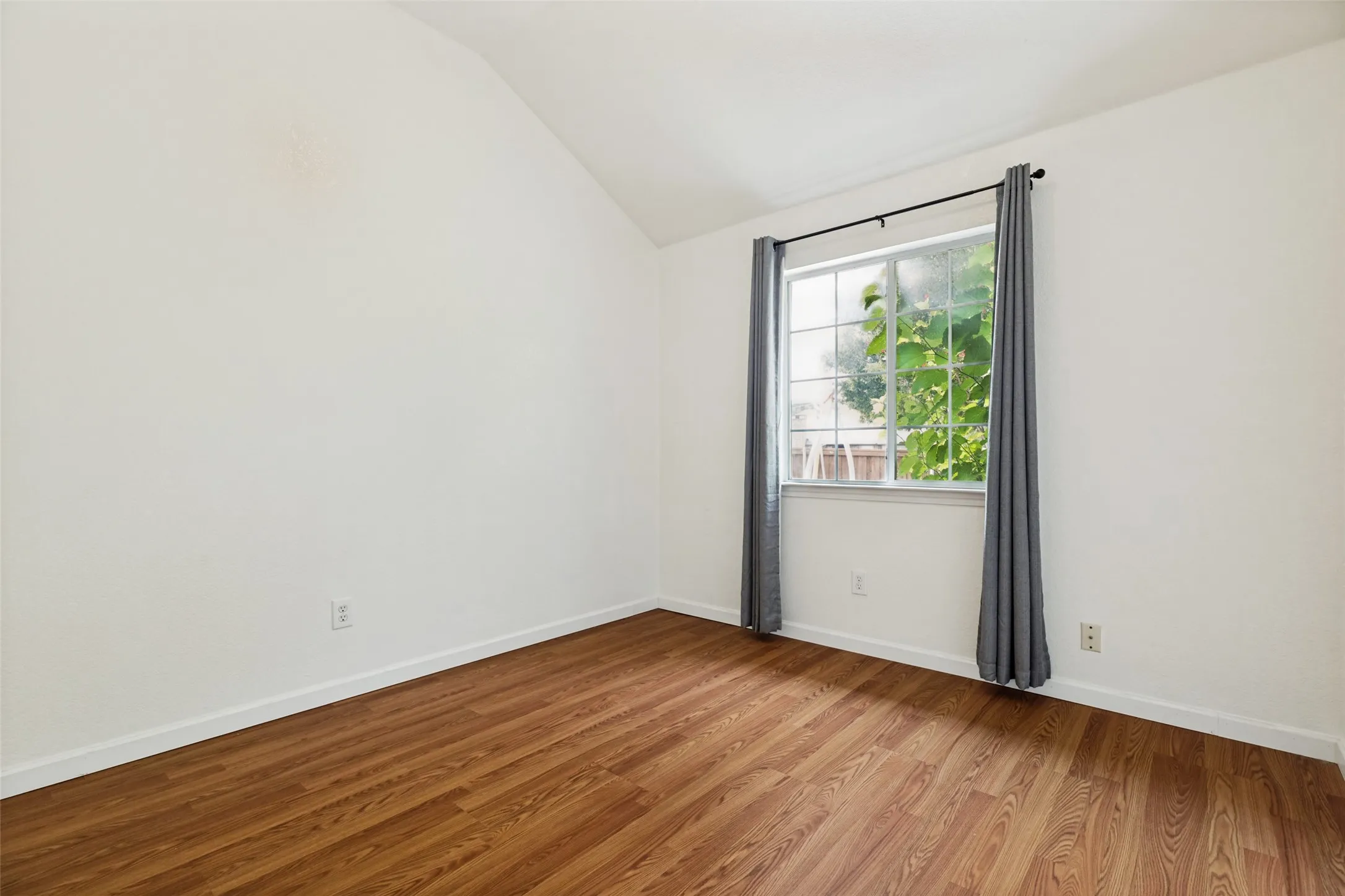 Vaulted ceiling, white walls, wood-finish flooring, and a single window