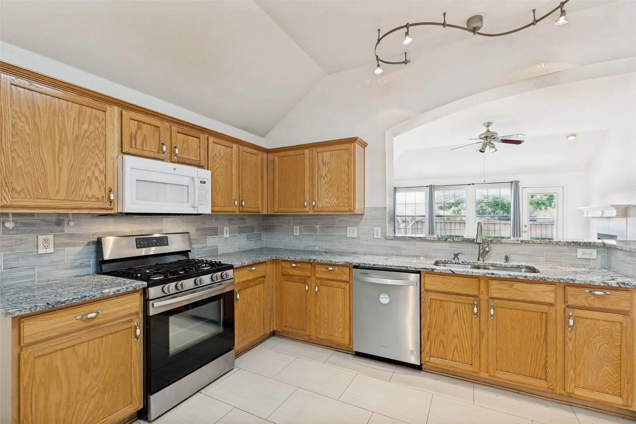 Kitchen with wood cabinetry, stainless steel appliances, granite-style countertops, and a gray subway tile backsplash