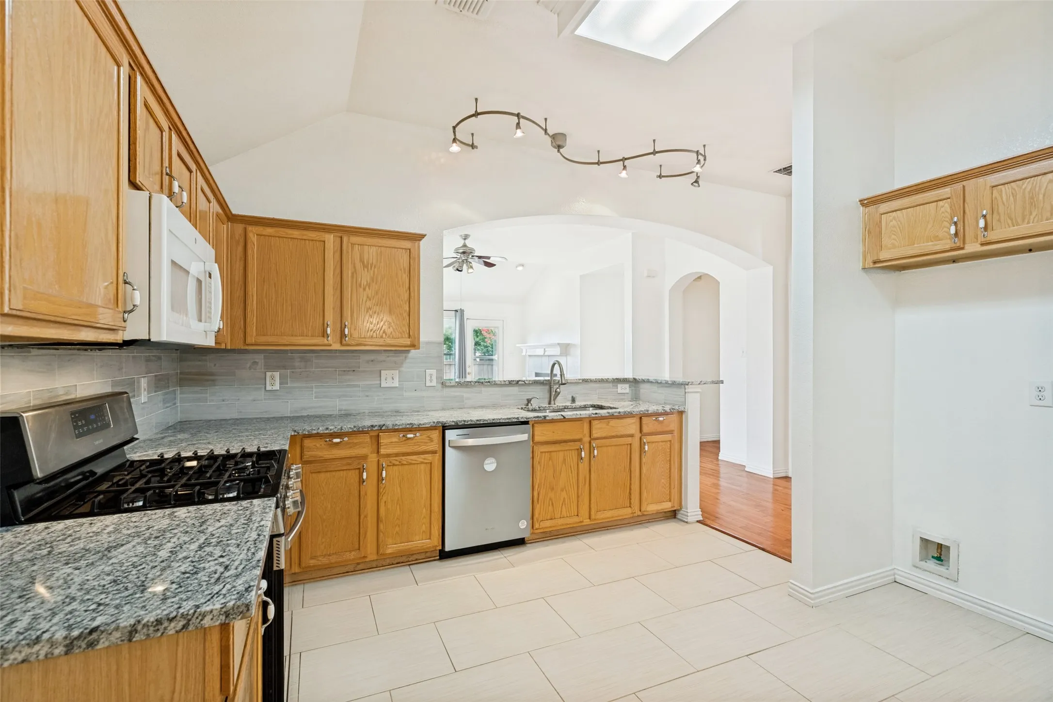 Kitchen featuring light wood cabinetry, white tile flooring, stainless steel appliances, and a skylight