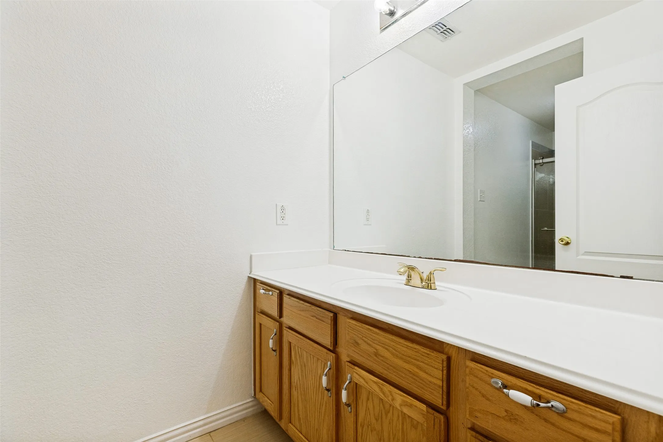 Vanity with wood cabinetry, integrated sink, and expansive wall-mounted mirror