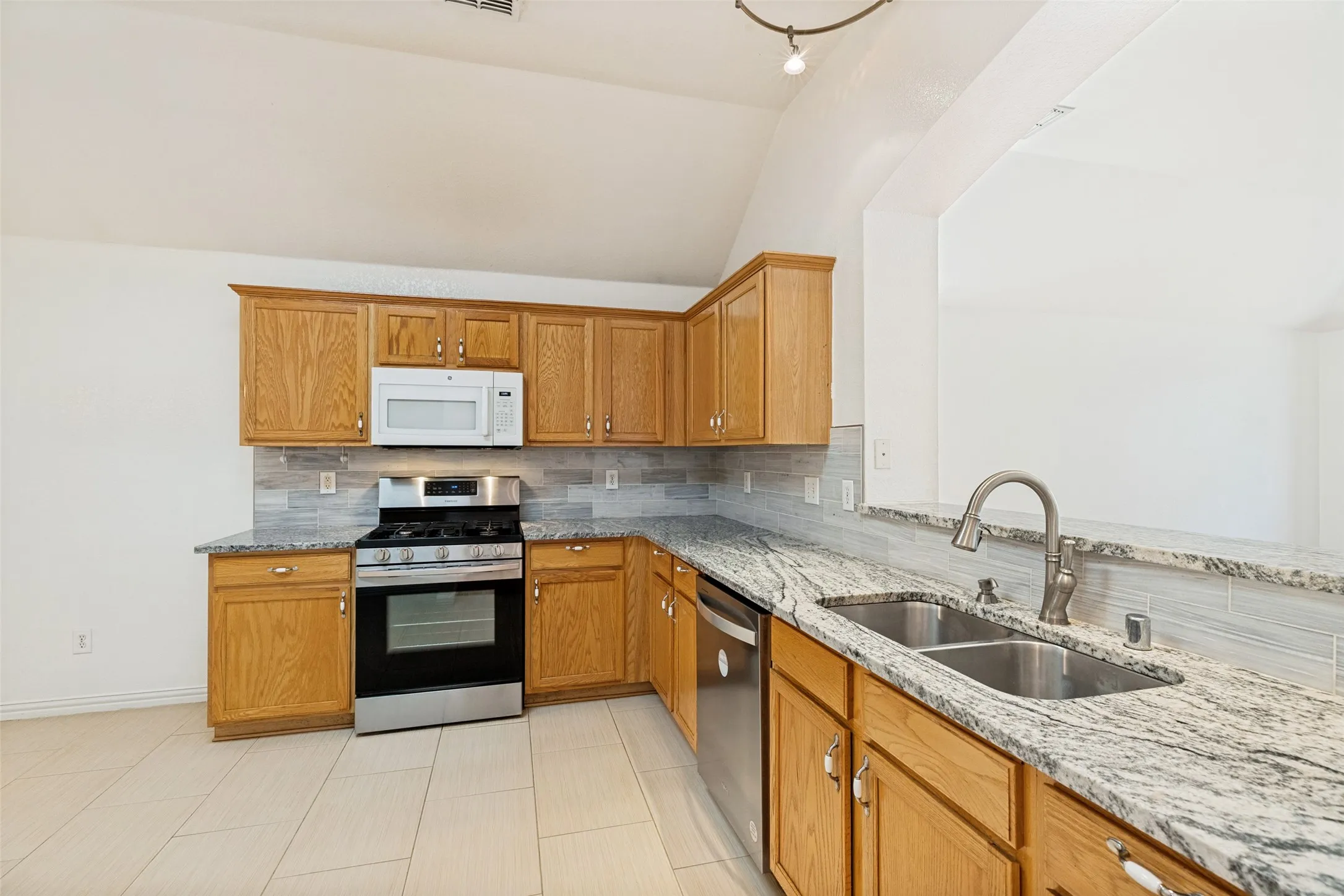 Kitchen featuring a vaulted ceiling, wood-finish cabinetry, stainless steel appliances, granite countertops, and a double basin sink