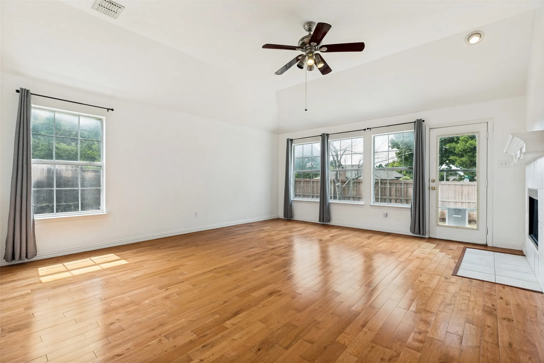 Vaulted ceilings, wood-finish flooring, ceiling fan with integrated lighting, multiple large windows, and a glass-paneled door