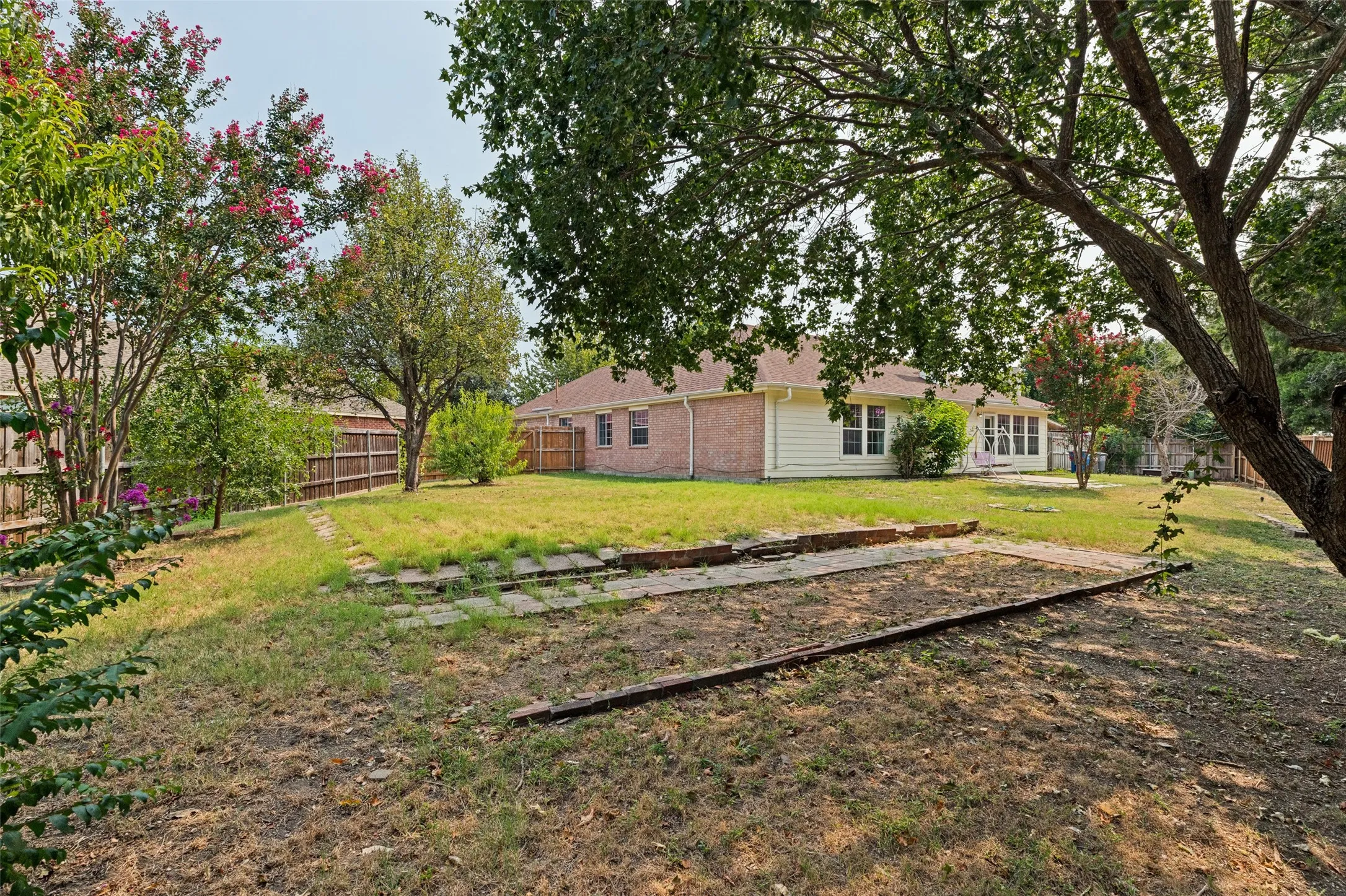 Expansive backyard featuring a wood fence, mature trees, and a brick and siding exterior
