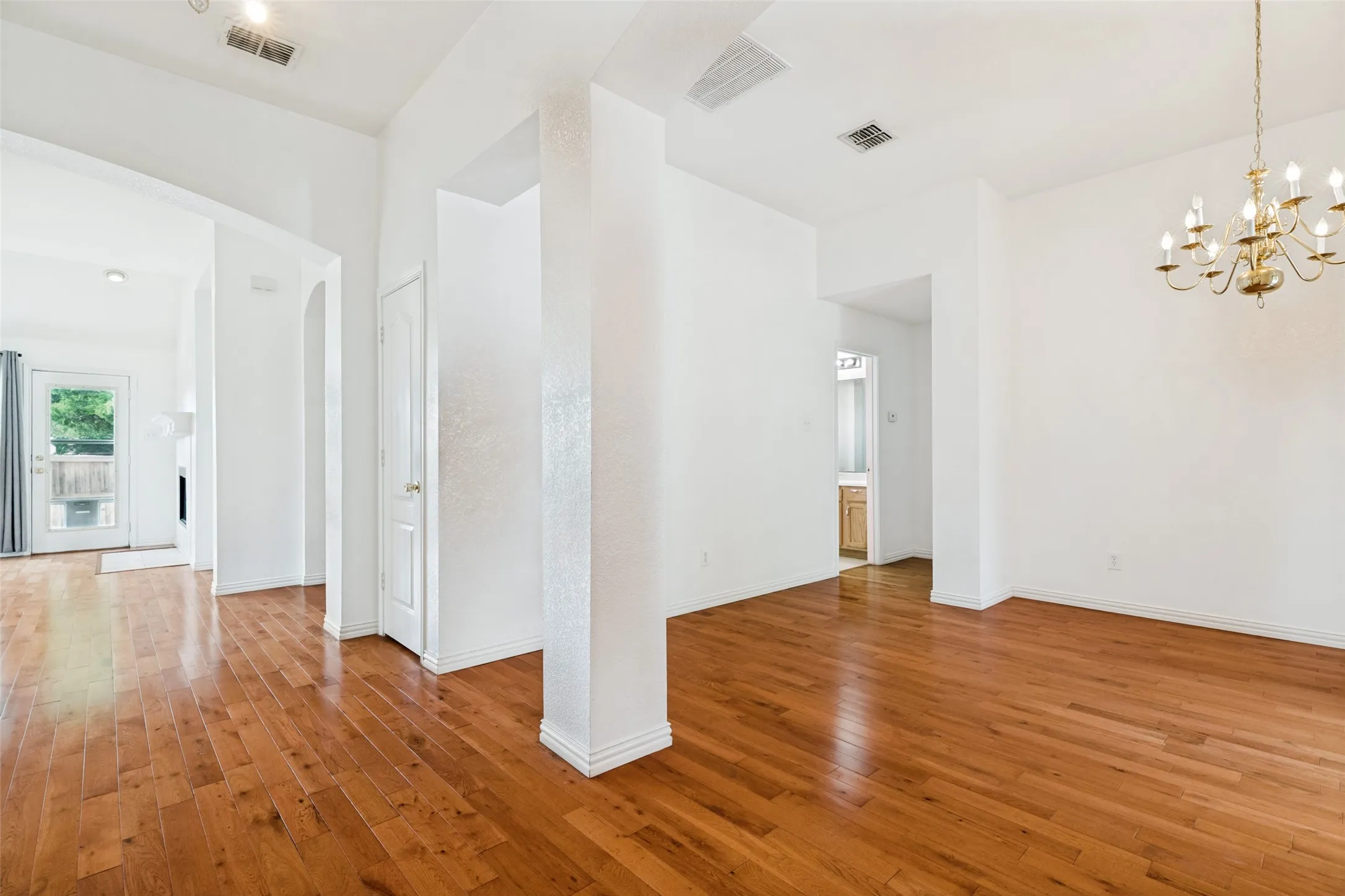 Hardwood flooring throughout, featuring a classic chandelier, recessed lighting, and a white paneled door