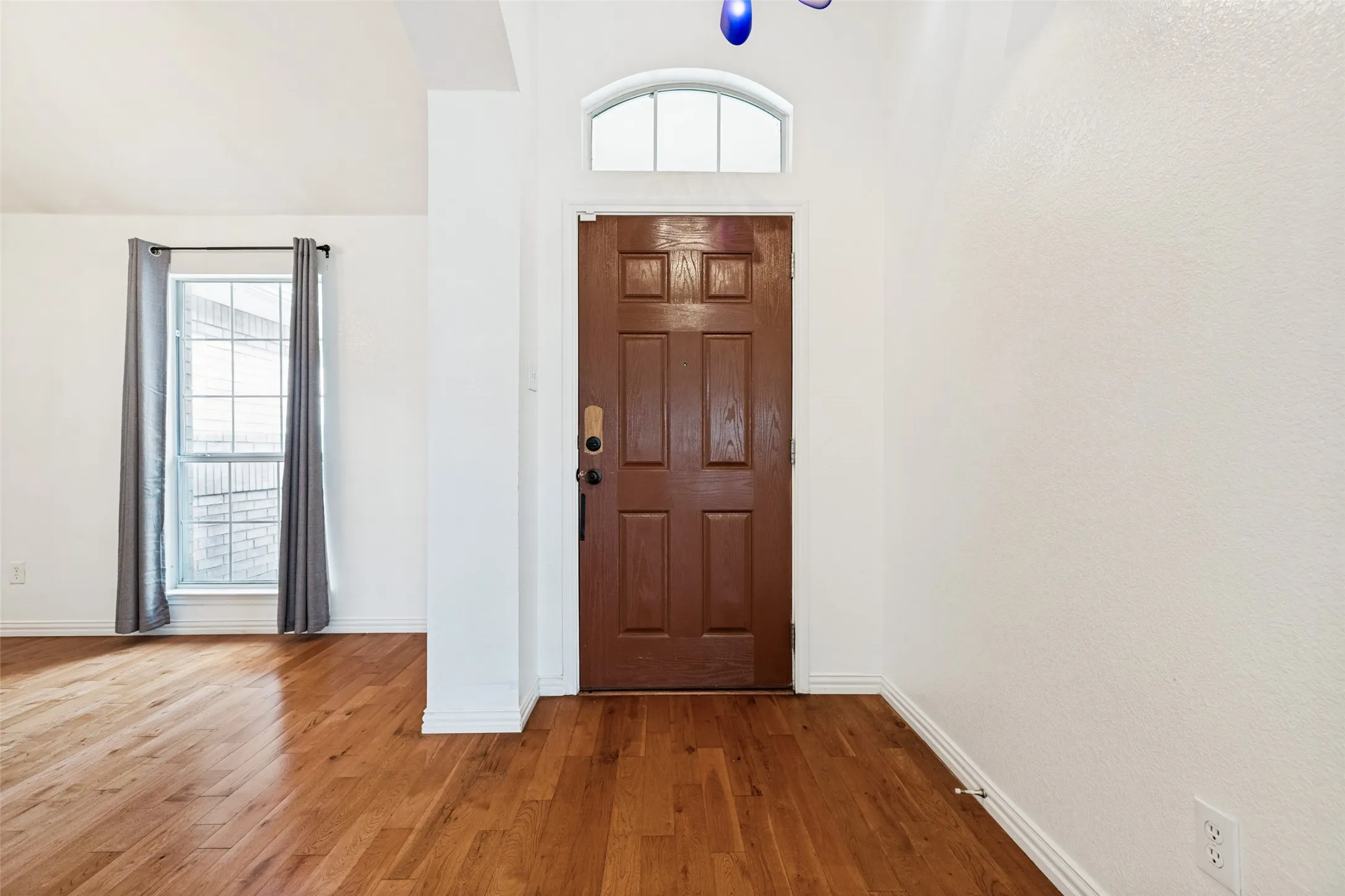 Paneled entry door with an arched transom window, wood-finish flooring, and white walls