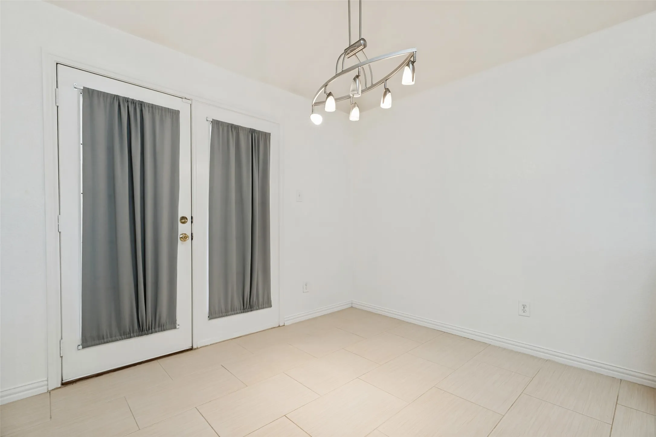 White walls featuring a contemporary linear chandelier and light-toned tile flooring